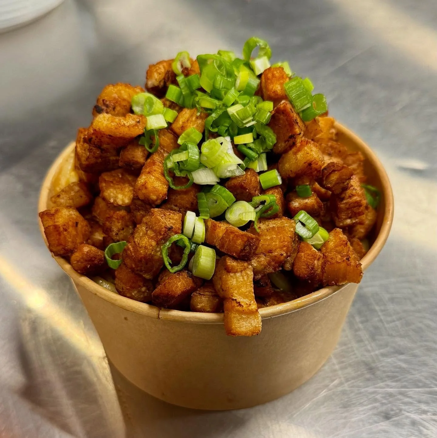 Fried diced pork topped with chopped green onions in a brown paper bowl.