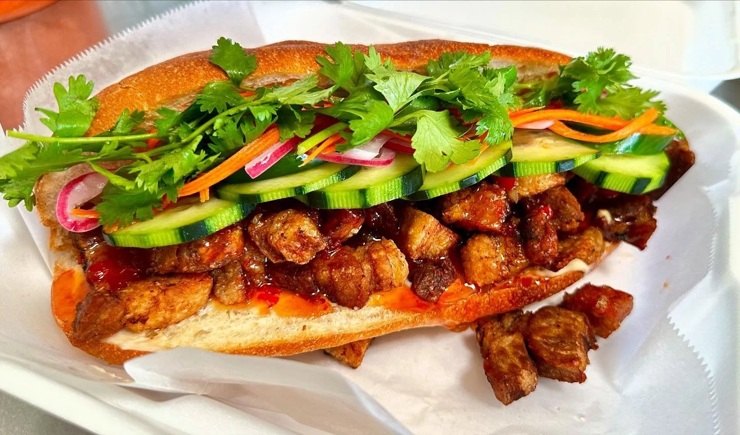 A Vietnamese banh mi sandwich filled with grilled pork, fresh cilantro, cucumber, carrots, pickled radish, and sliced red onion in a baguette.