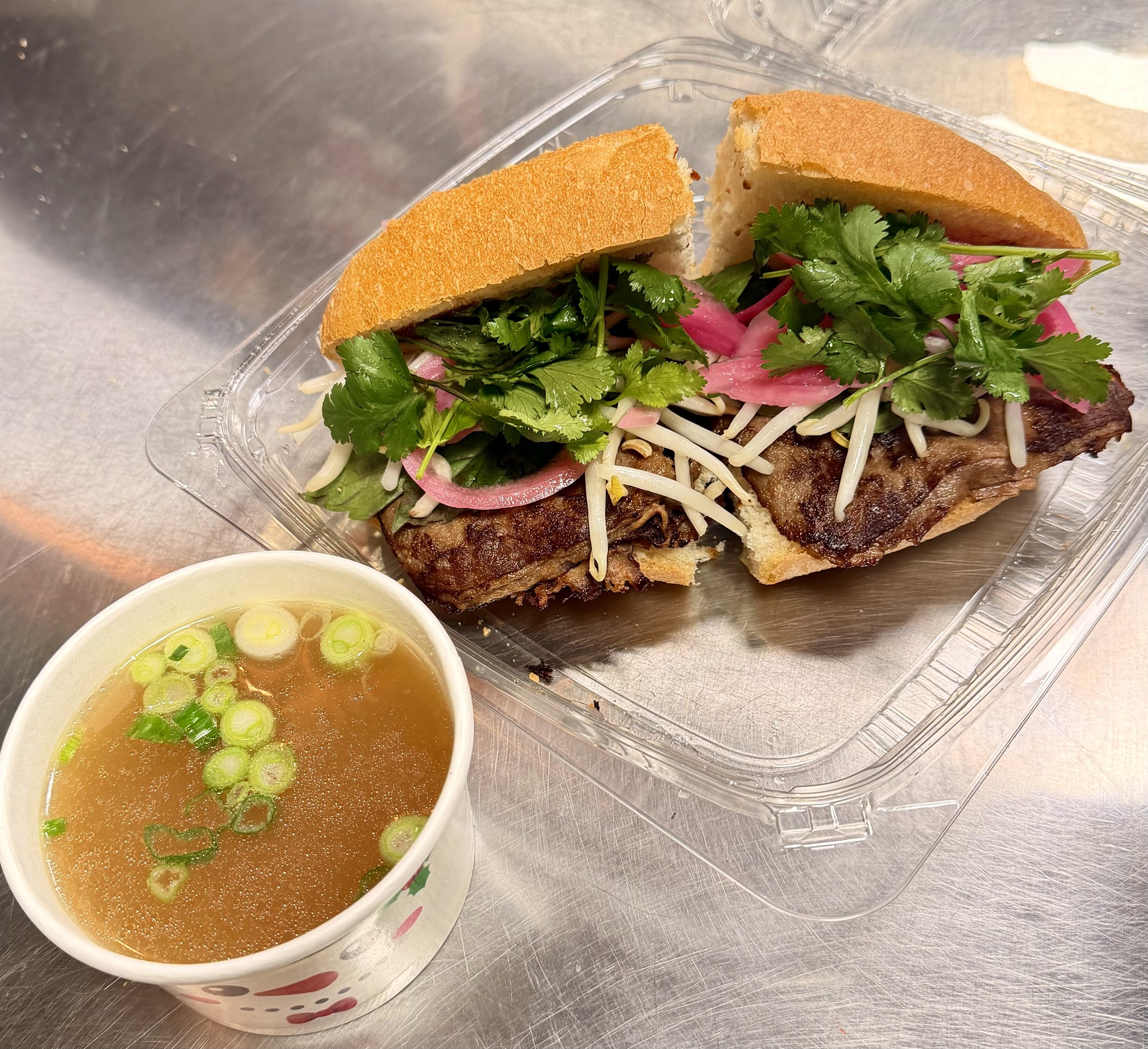 Barbecue pork sandwich with cilantro, pickled onions, and shredded cheese on a bun, served with a cup of green onion soup.