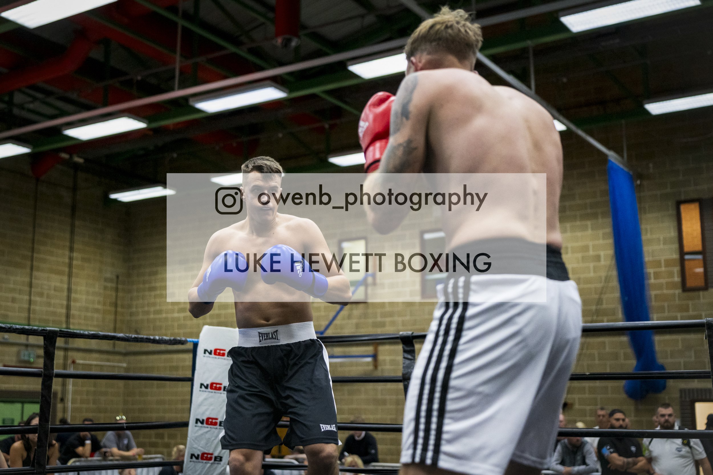 Two shirtless men boxing in a ring with spectators watching.