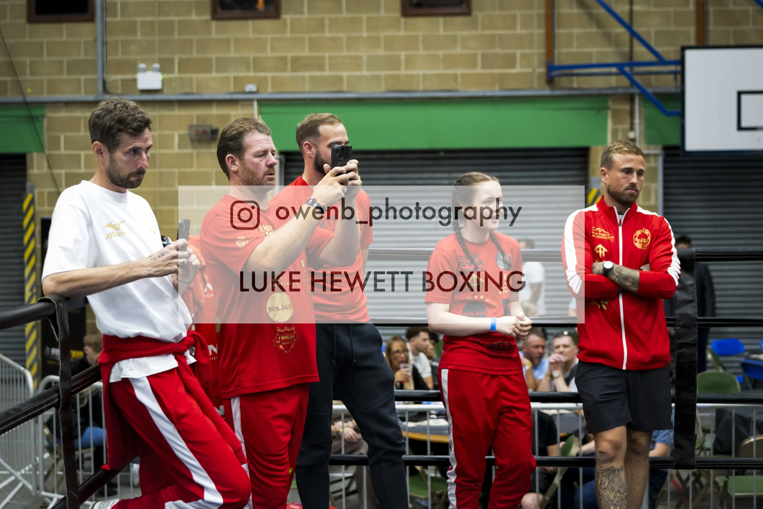 A group of people standing indoors, including men and a woman, some wearing red sports attire, at a boxing event or match.