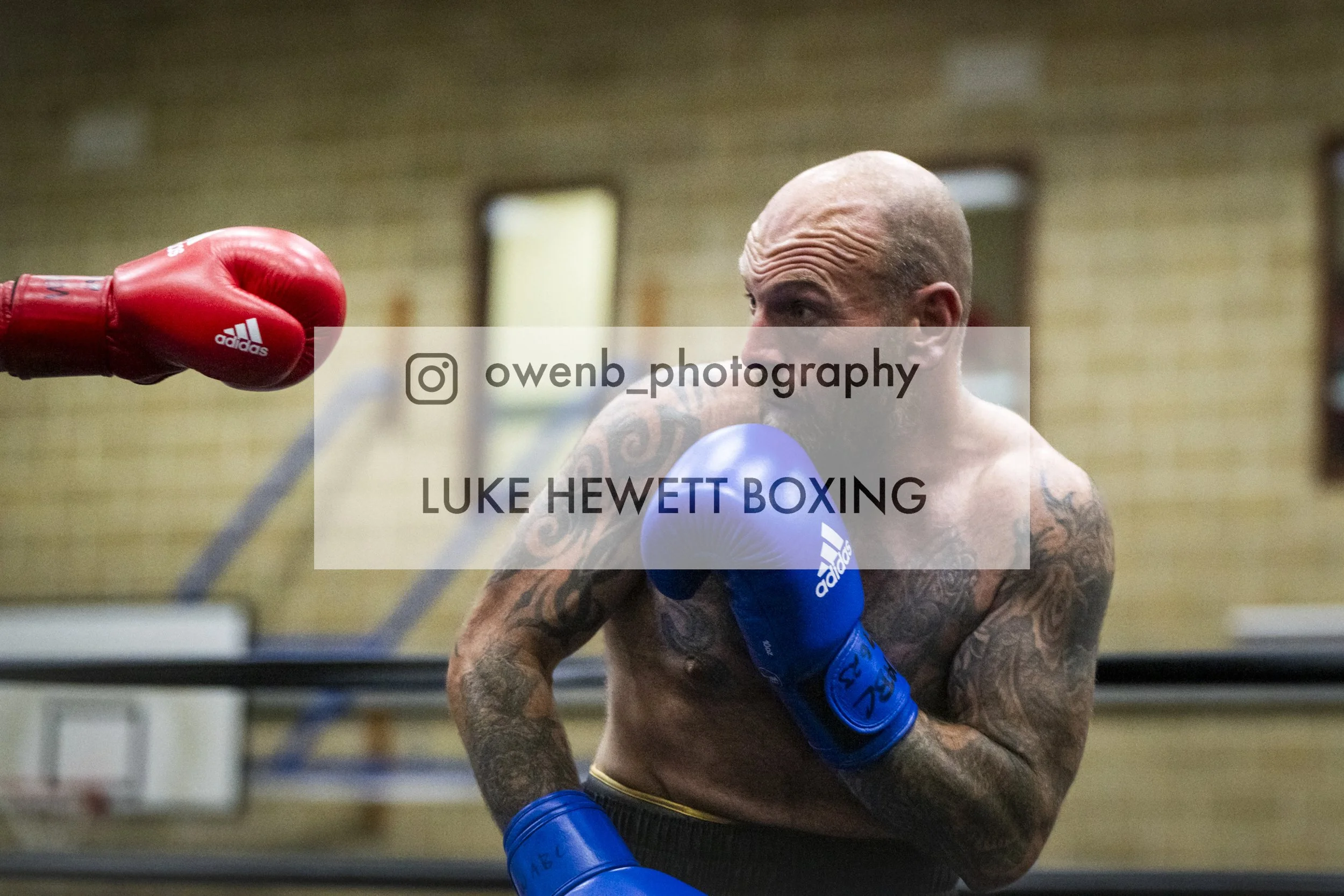 Boxer in blue gloves and shorts sparring with a punch from an opponent in red gloves in a gym setting.