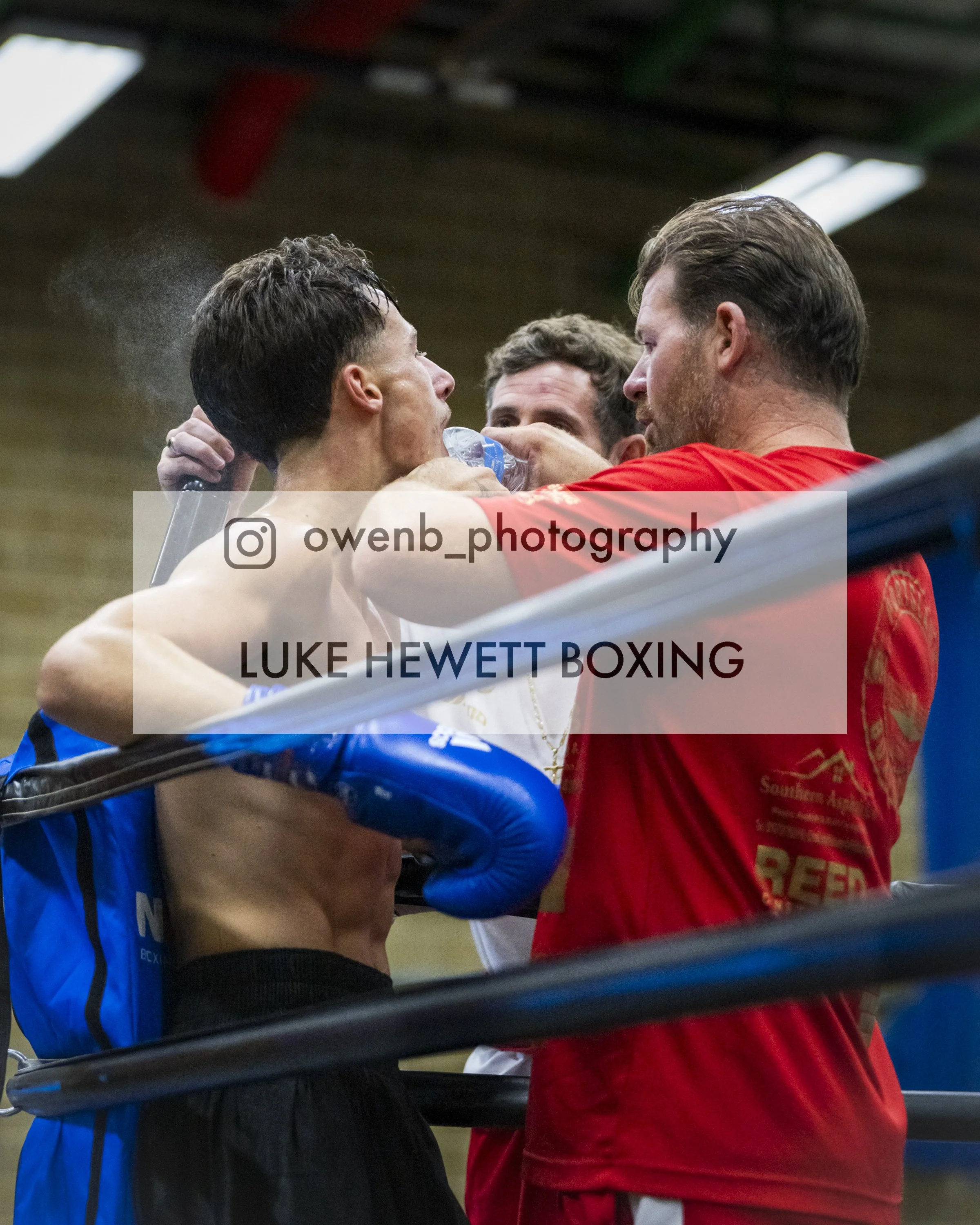 Boxer in the ring receiving water from a man in a red shirt, with another person in the background.