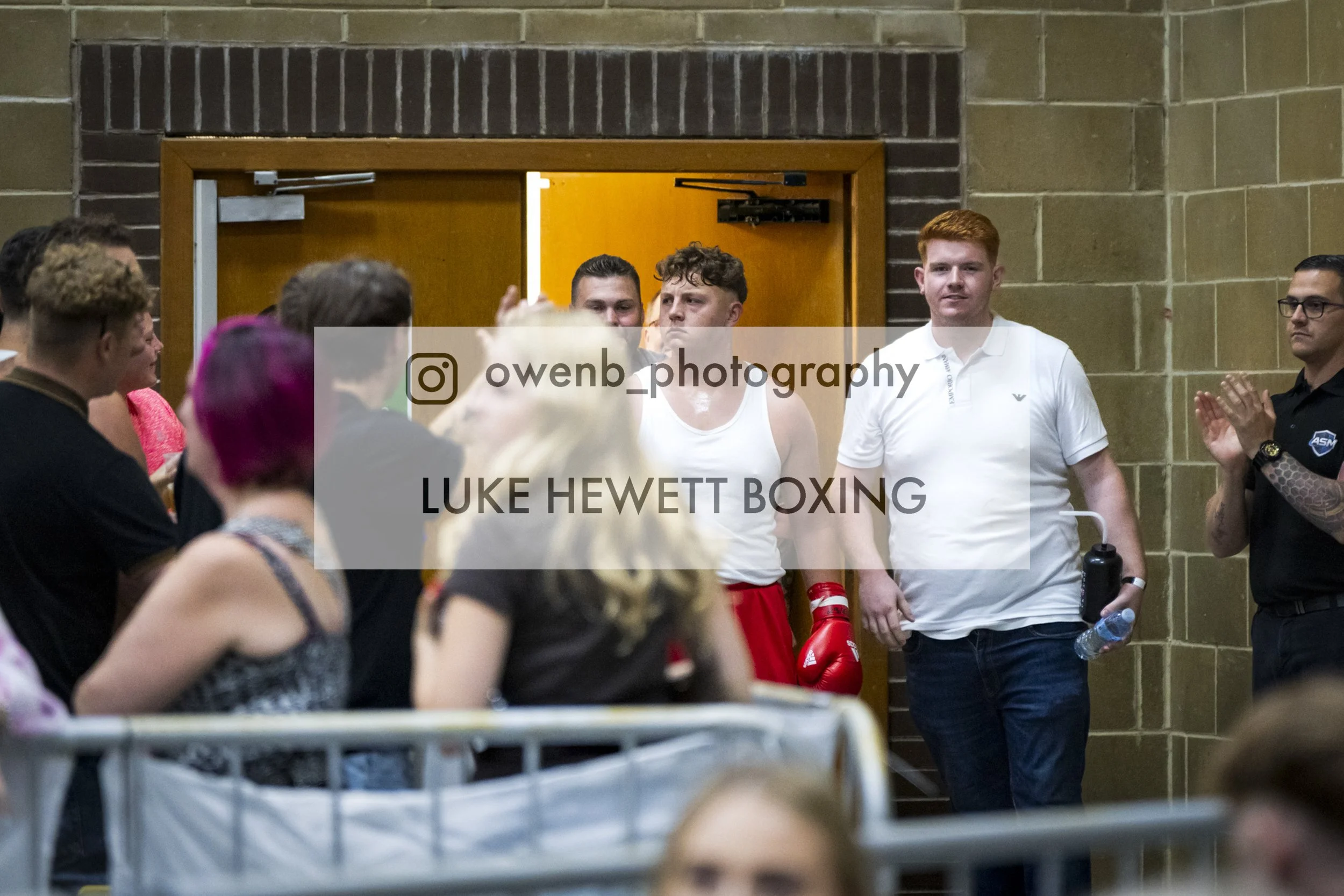 Boxing weigh-in or face-off event with fighters and spectators in a gym-like setting.