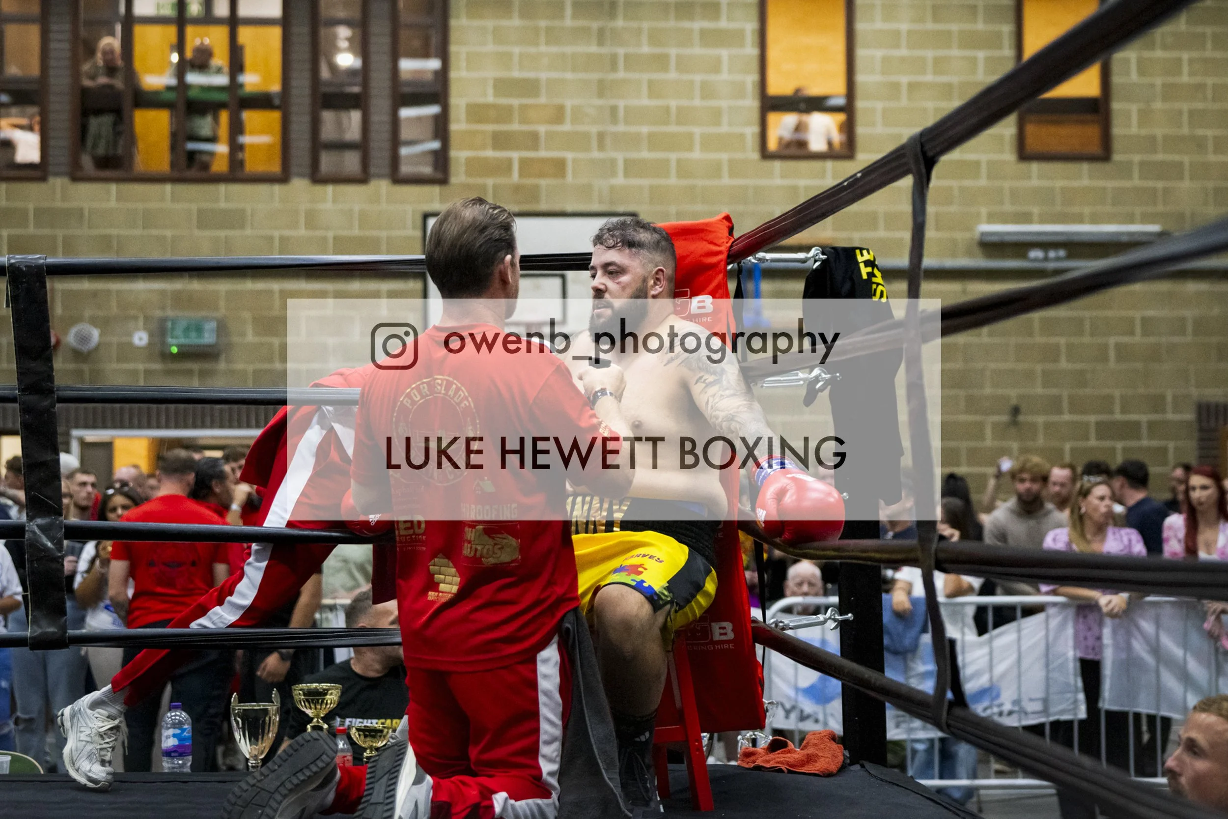 Boxer Luke Hewett receiving medical attention in his corner during a boxing match, with a crowd watching in the background.