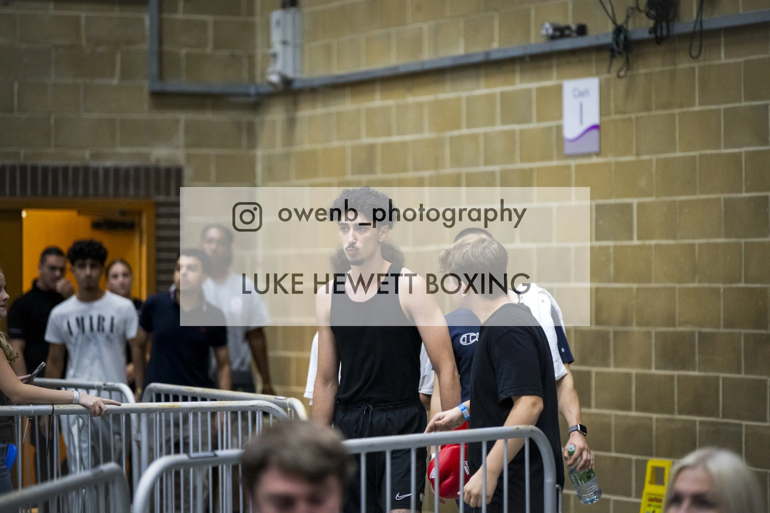 Boxer Luke Hewett in a boxing gym surrounded by spectators, wearing boxing gloves and preparing for a match.