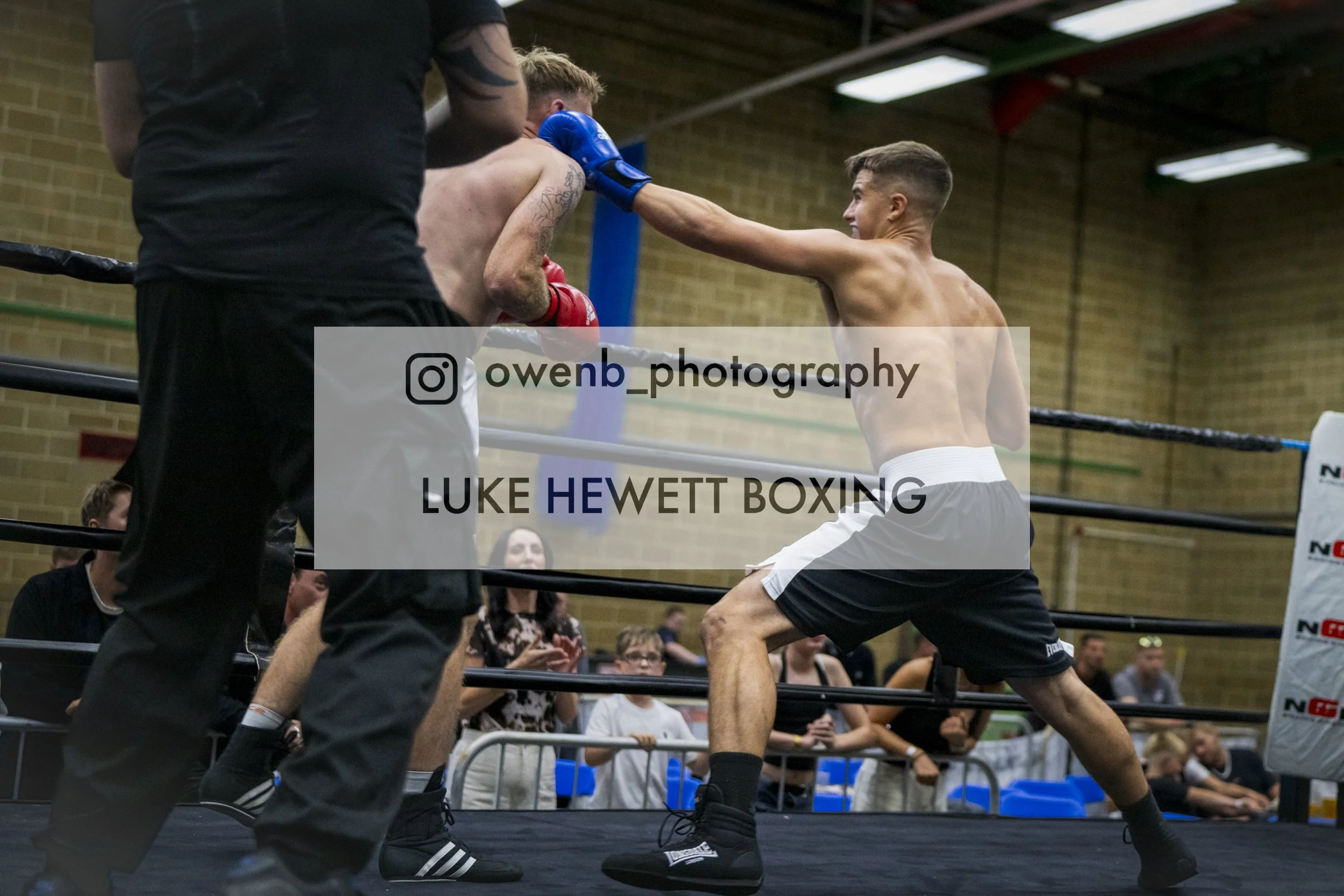 A boxer throws a punch at his opponent in a boxing ring during a match, with spectators watching in the background.