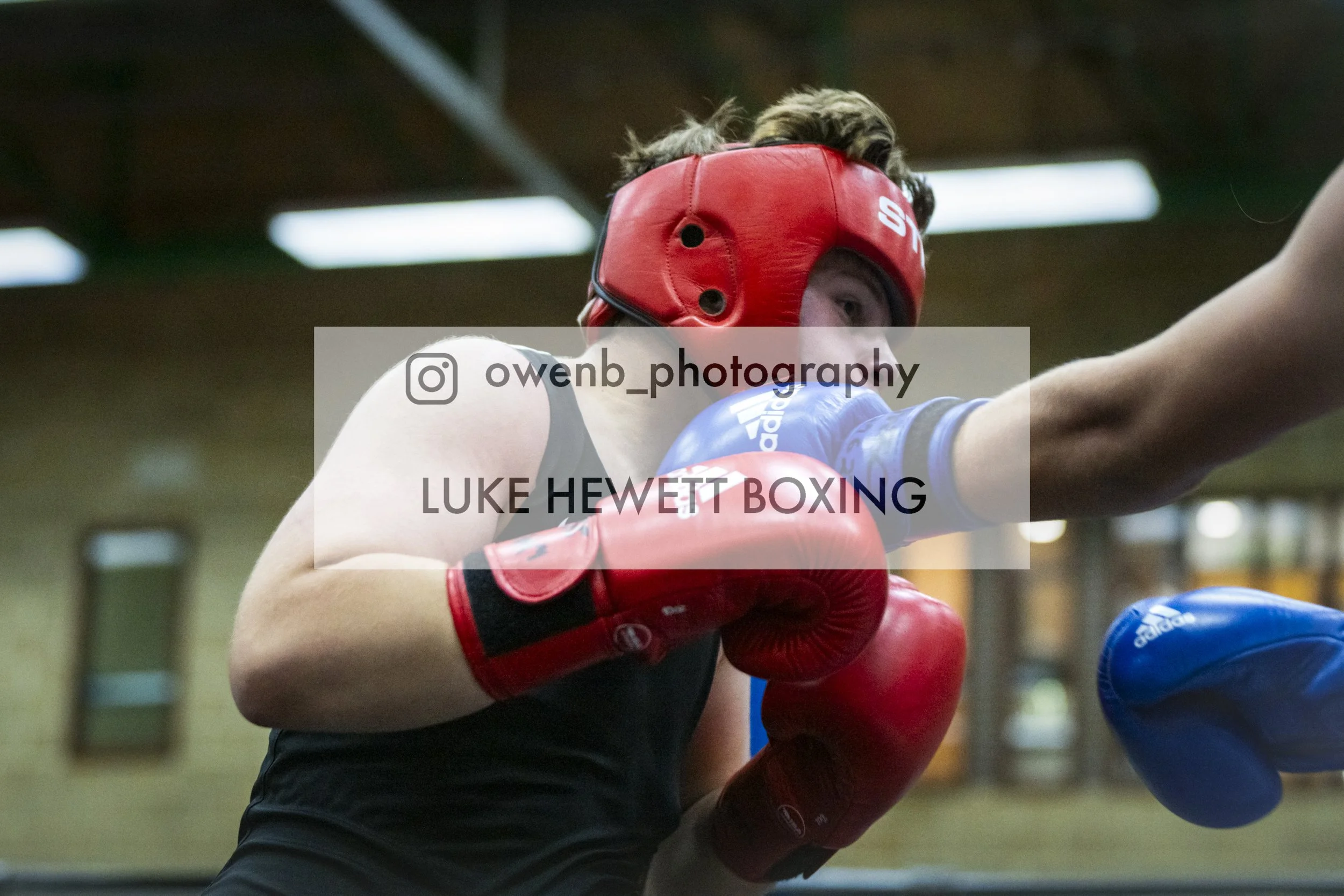 Boxer wearing red headgear and gloves throwing a punch during a boxing match in a gym