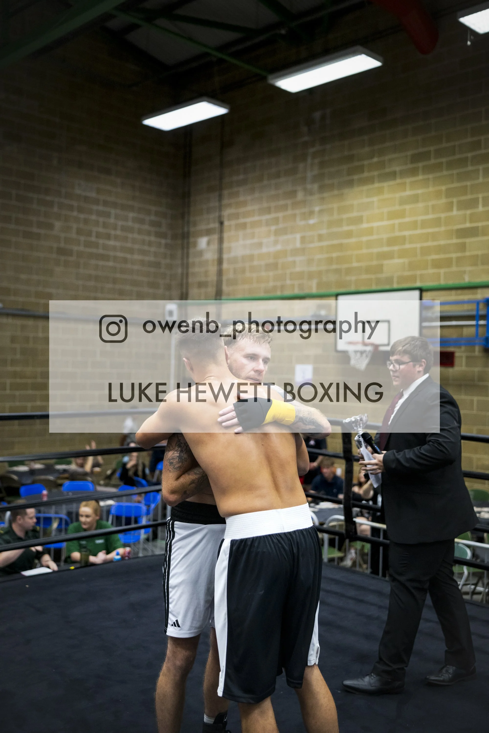 Boxers hugging in the boxing ring after a match, with fans and officials nearby.
