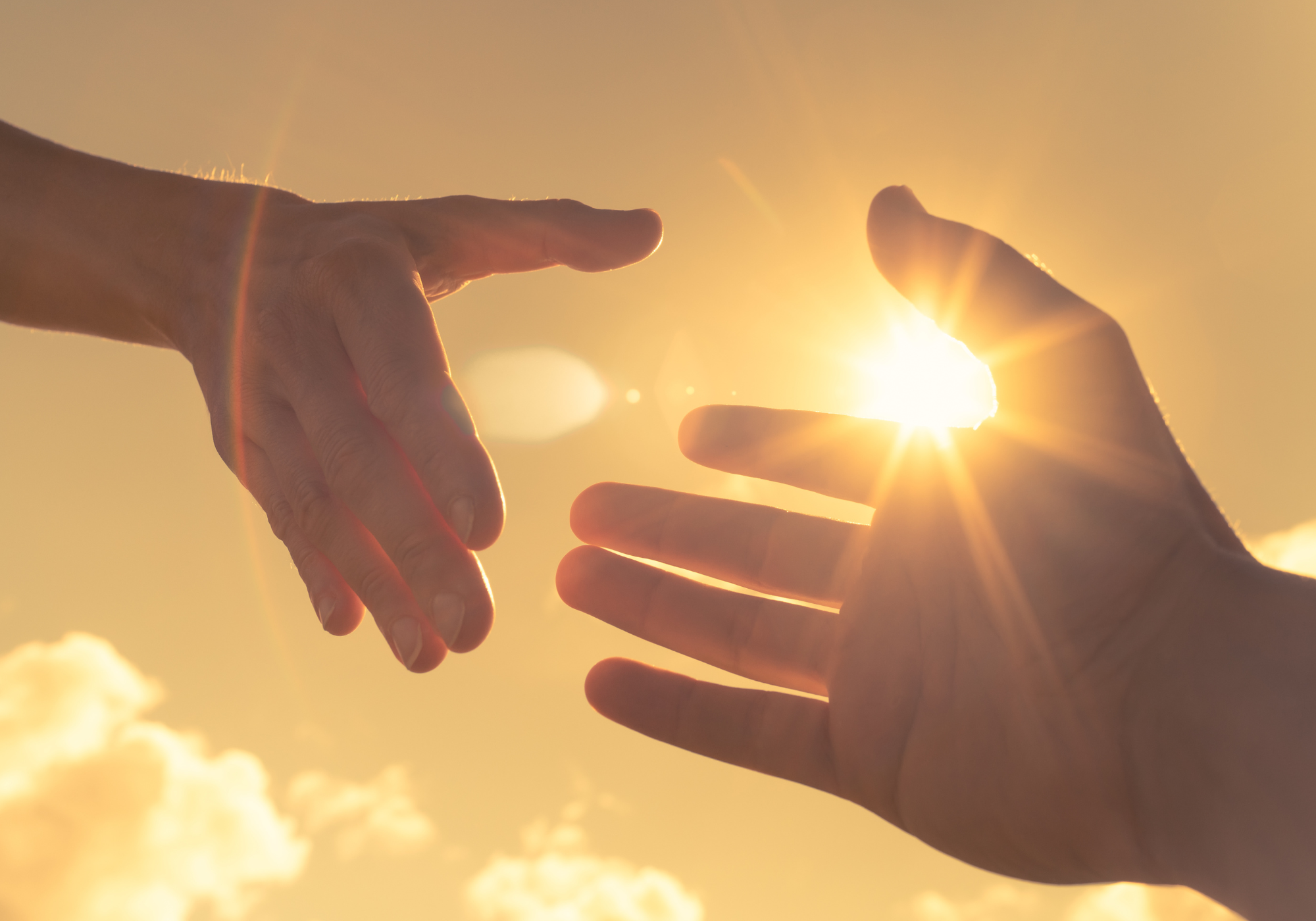 Two hands reaching towards each other with the sun shining between them in a bright sky.