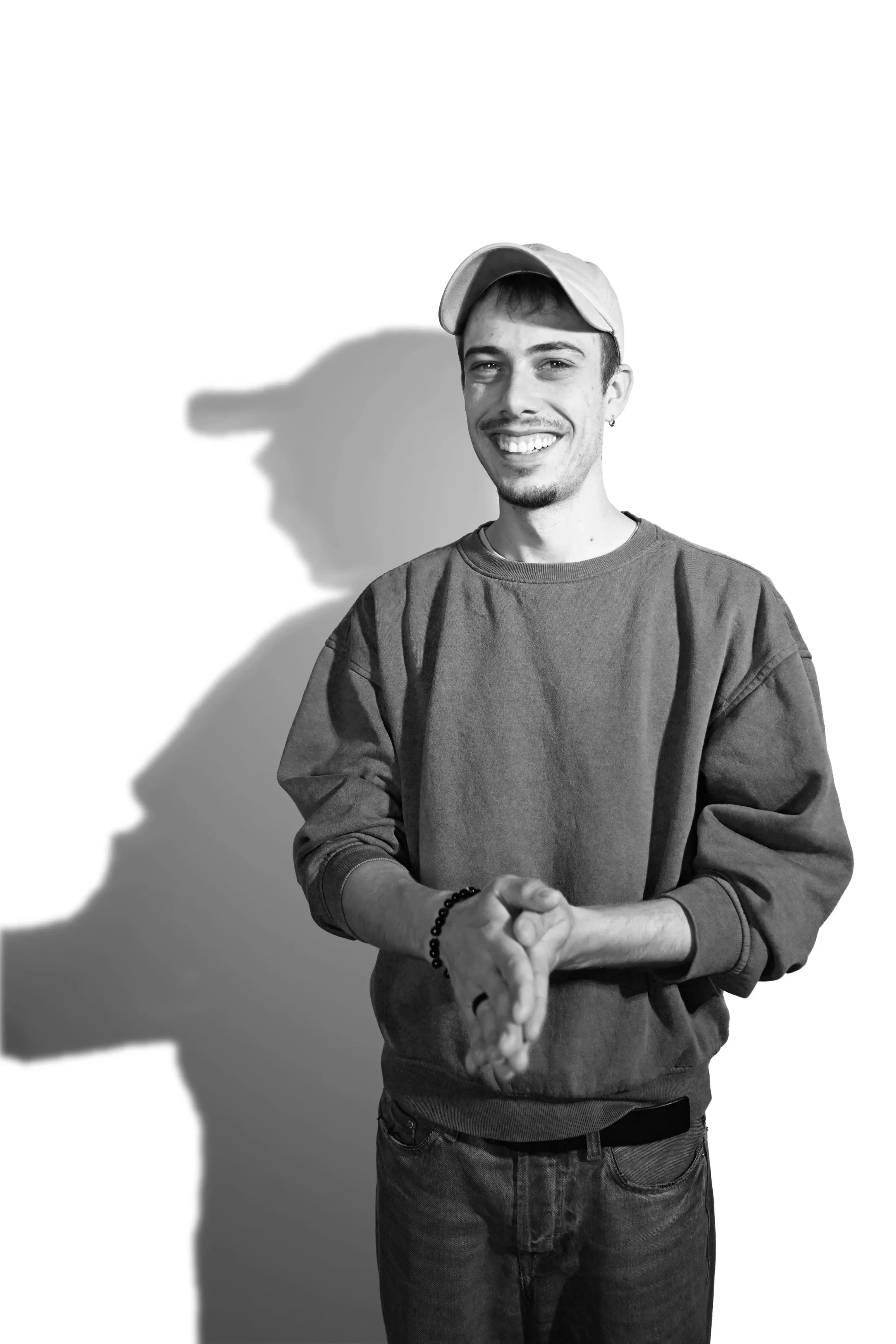 Schwarz-weißes Porträt eines lächelnden Mannes mit Baseballkappe und Sweatshirt vor weißem Hintergrund