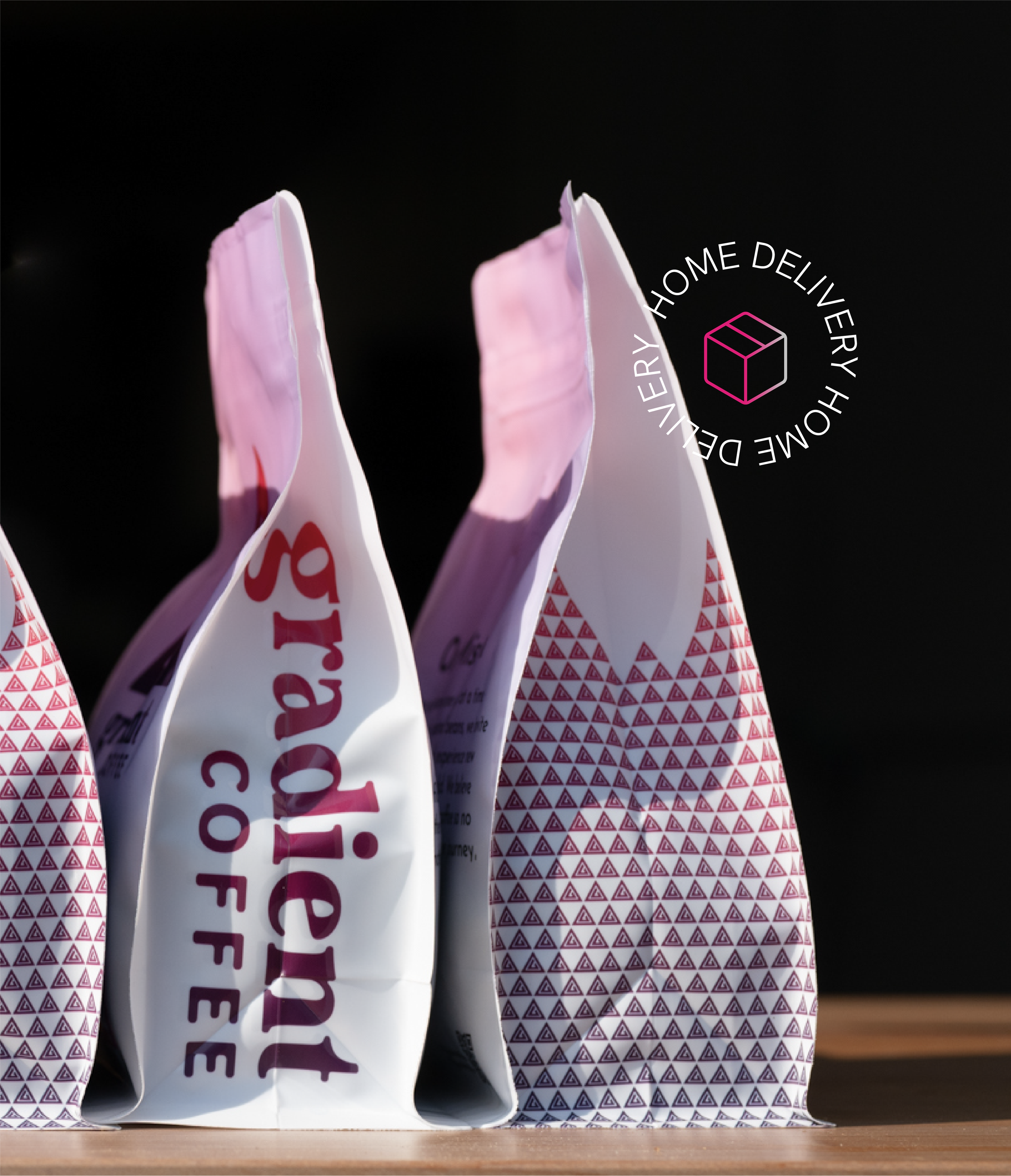 Gradient Coffee bags on a wooden surface with pink and patterned packaging, set against a dark background with a home delivery icon.