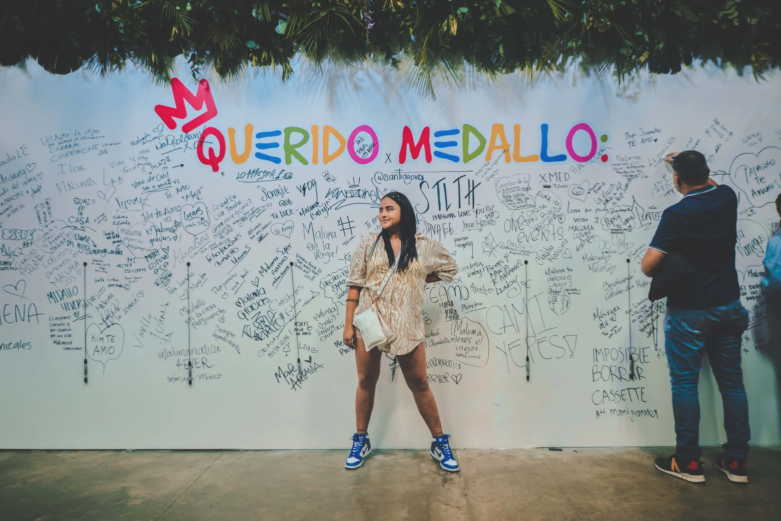People writing on a large wall with the words 'Querido Medallo' at the top, colorful letters, at an event or gathering.