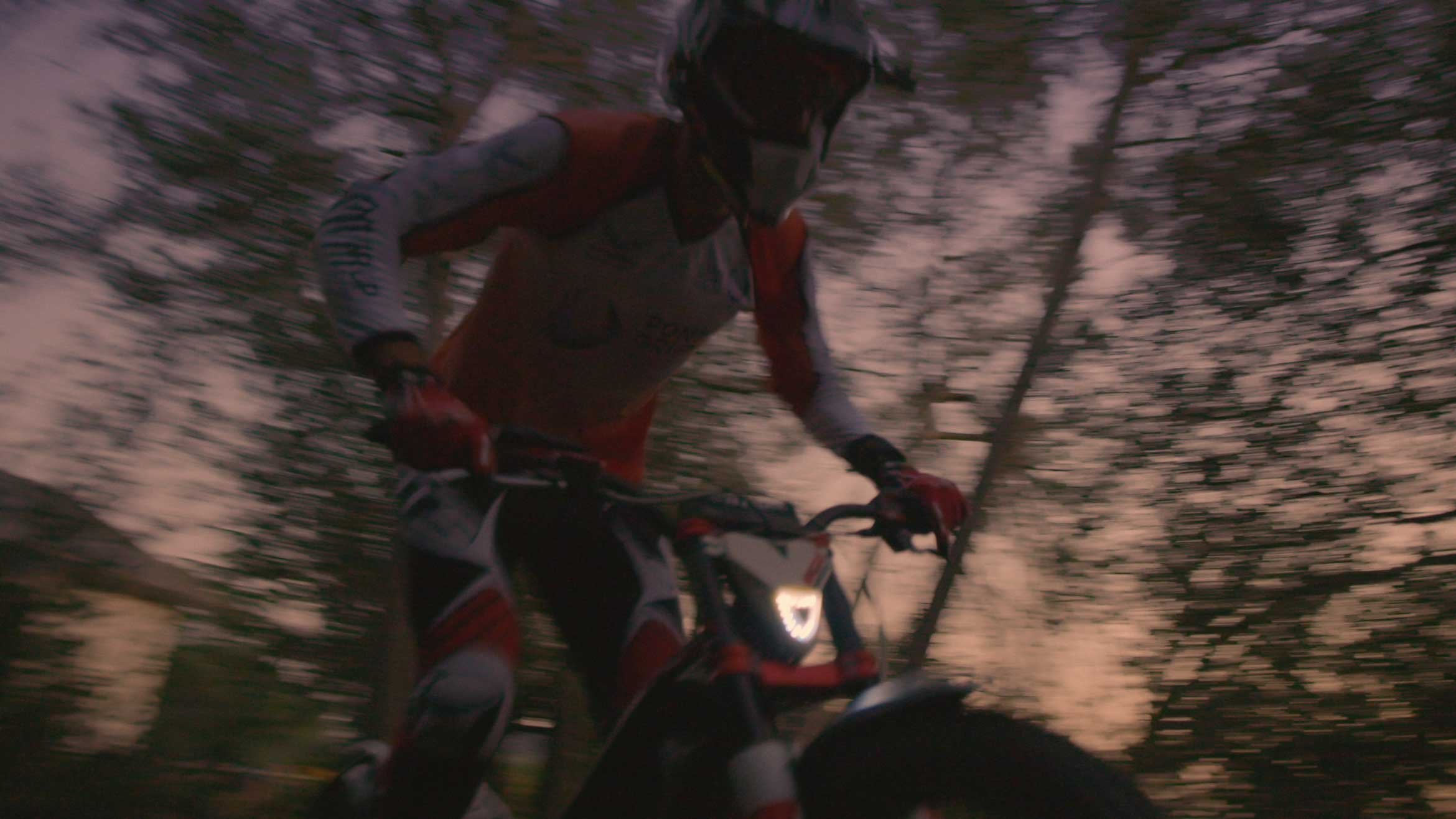 A person riding a mountain bike through a wooded area at dusk, with trees blurred in the background wearing LS2 Helmets.