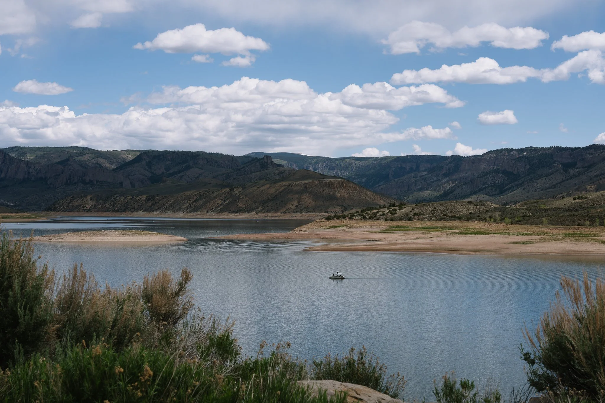 A lake with a boat floating on the water, surrounded by mountains and a partly cloudy sky.