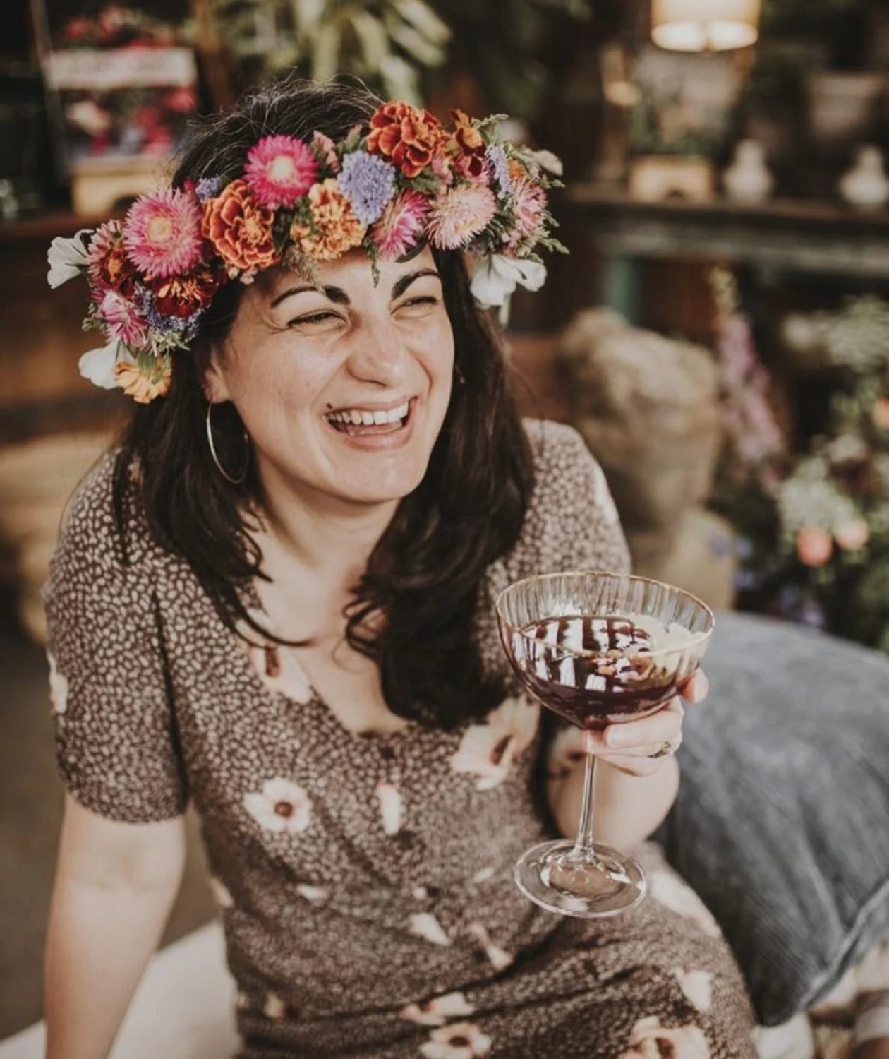 Woman wearing a flower crown and holding a glass of red wine.