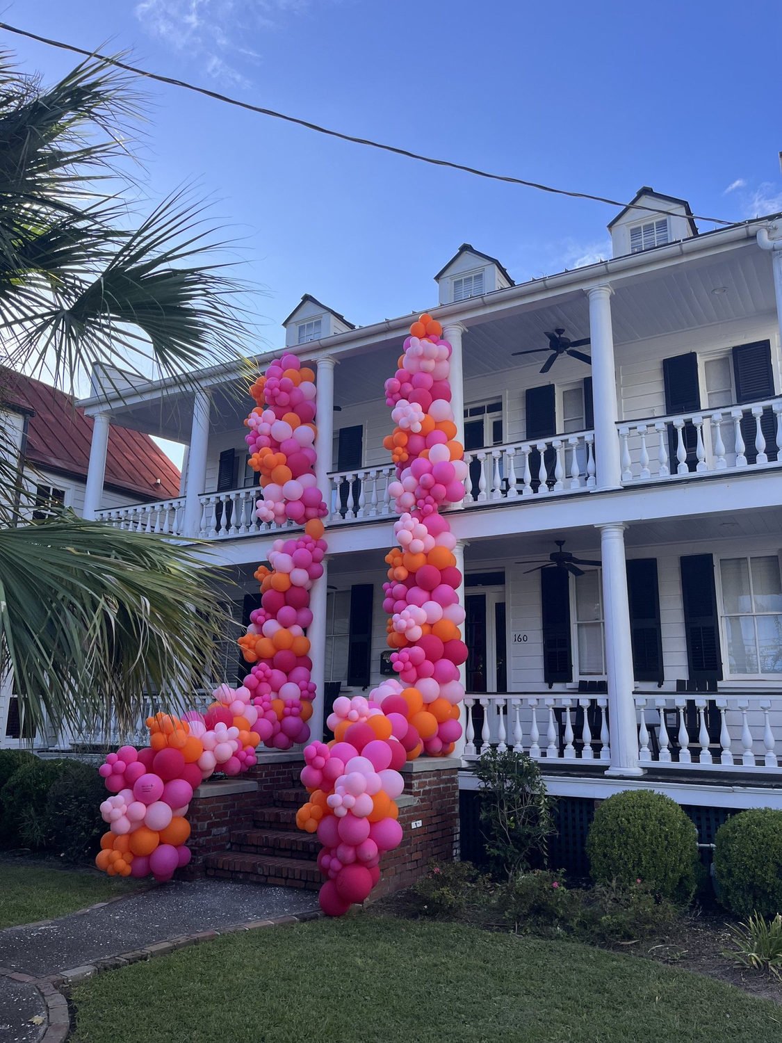 Pink and orange balloon garland outside a white house