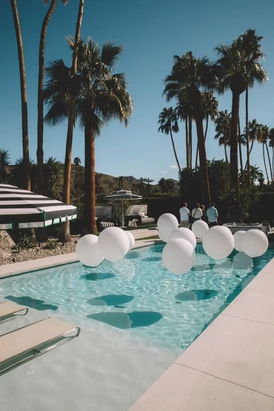 White balloons floating in a palm-lined swimming pool.