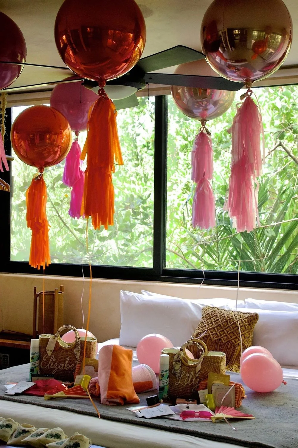 Pink and orange bachelorette welcome gifts arranged beneath oversized metallic balloons and tassels.