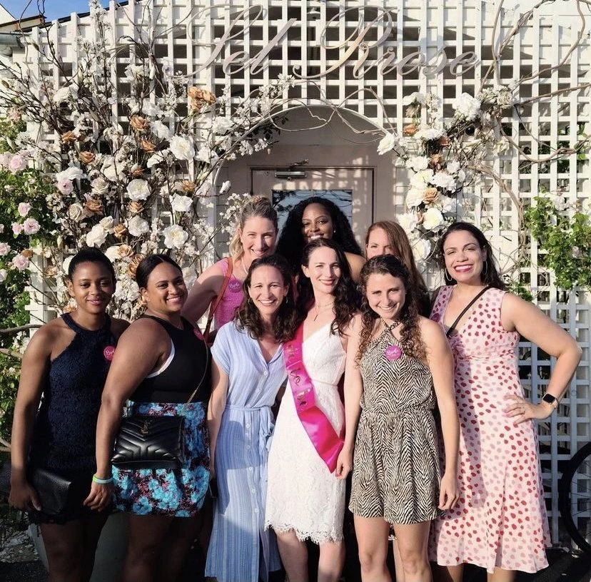 Bachelorette group posing beneath a floral arch outside a Hamptons venue.