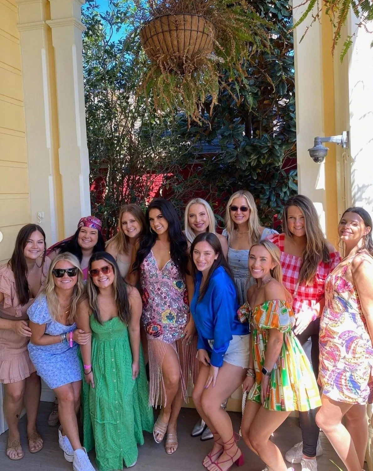 Bachelorette group in colorful dresses beneath a hanging planter in a New Orleans courtyard.