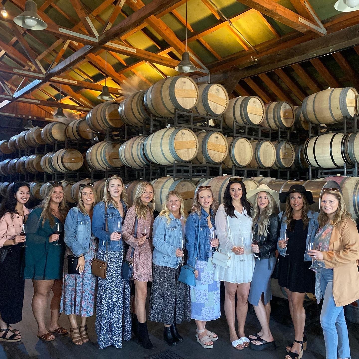 Bachelorette group posing beside stacked wine barrels in a Napa winery.