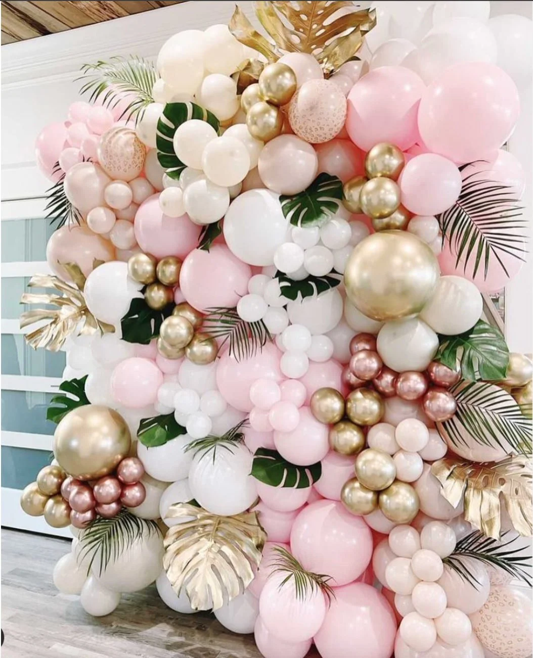 Pink, white and gold balloon wall decorated with tropical leaves.