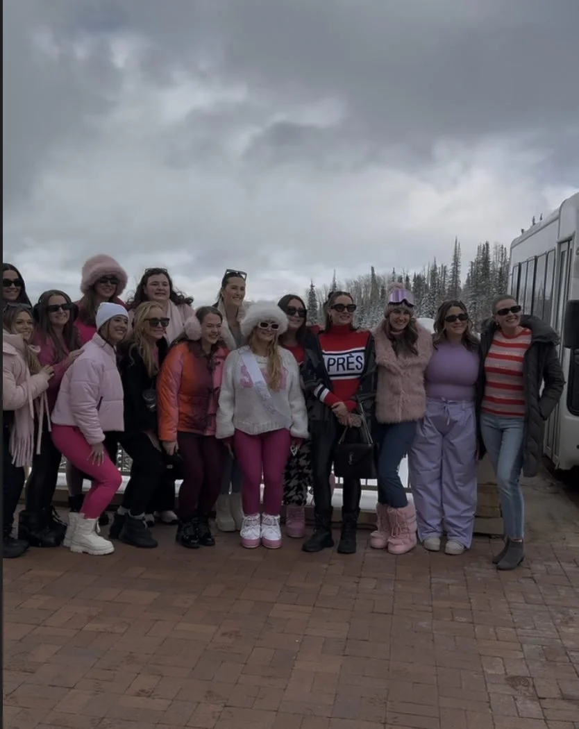 Bachelorette group in pink and white winter outfits posing together outdoors in Park City.