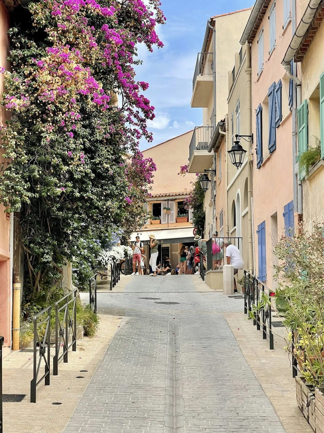 Narrow Saint-Tropez street lined with pastel buildings and flowering vines.