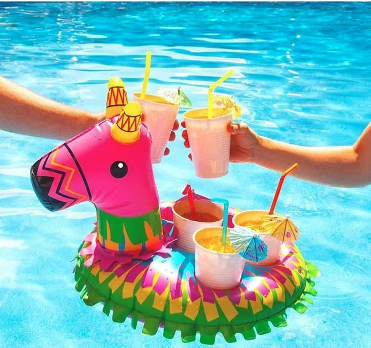Hands holding colorful drinks beside a floating llama drink holder in a pool.