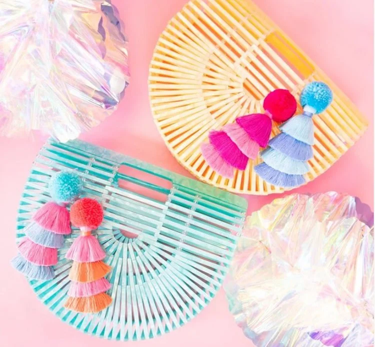 Pastel fan-shaped clutches decorated with colorful pom-pom tassels.