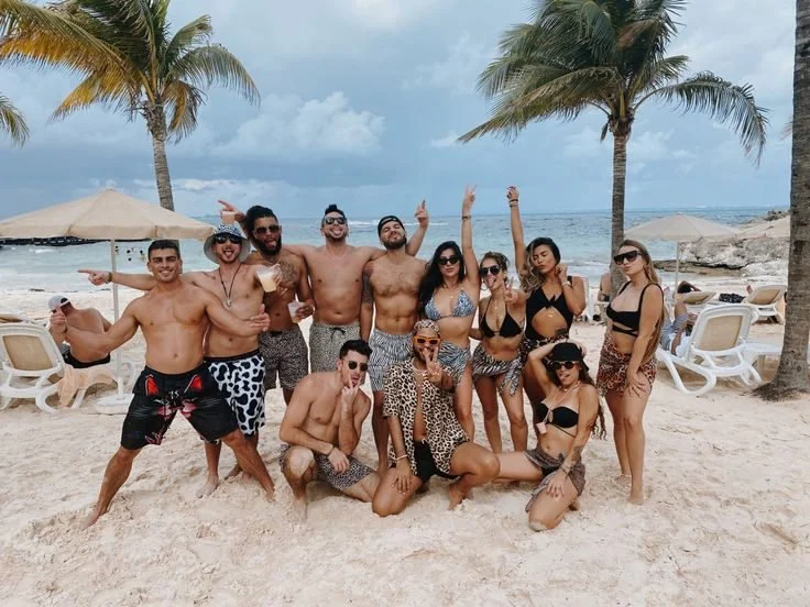 Joint bachelor and bachelorette group posing together on a palm-lined beach.
