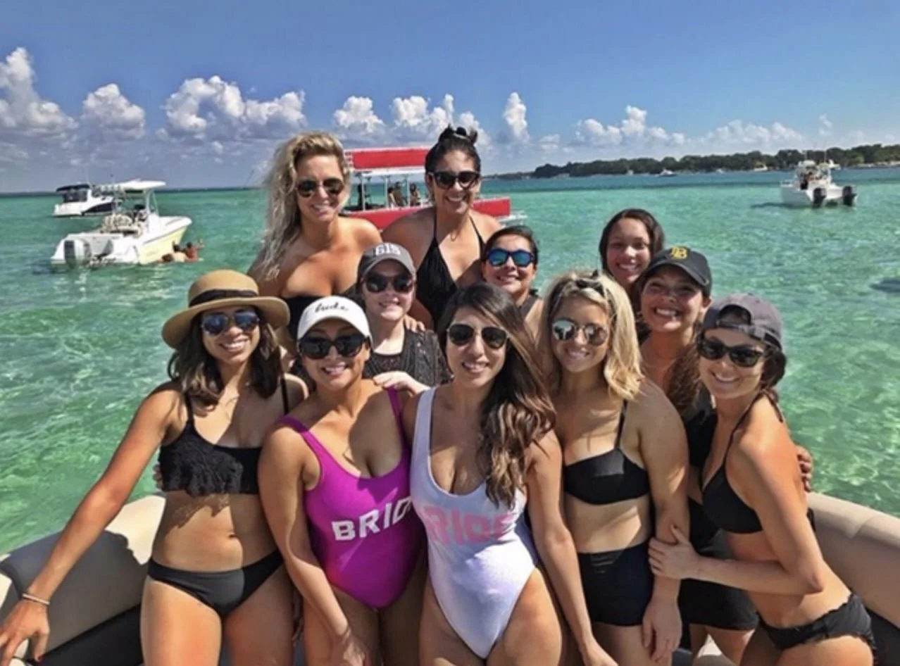 Bachelorette group in swimsuits posing together on a boat in clear Florida water.