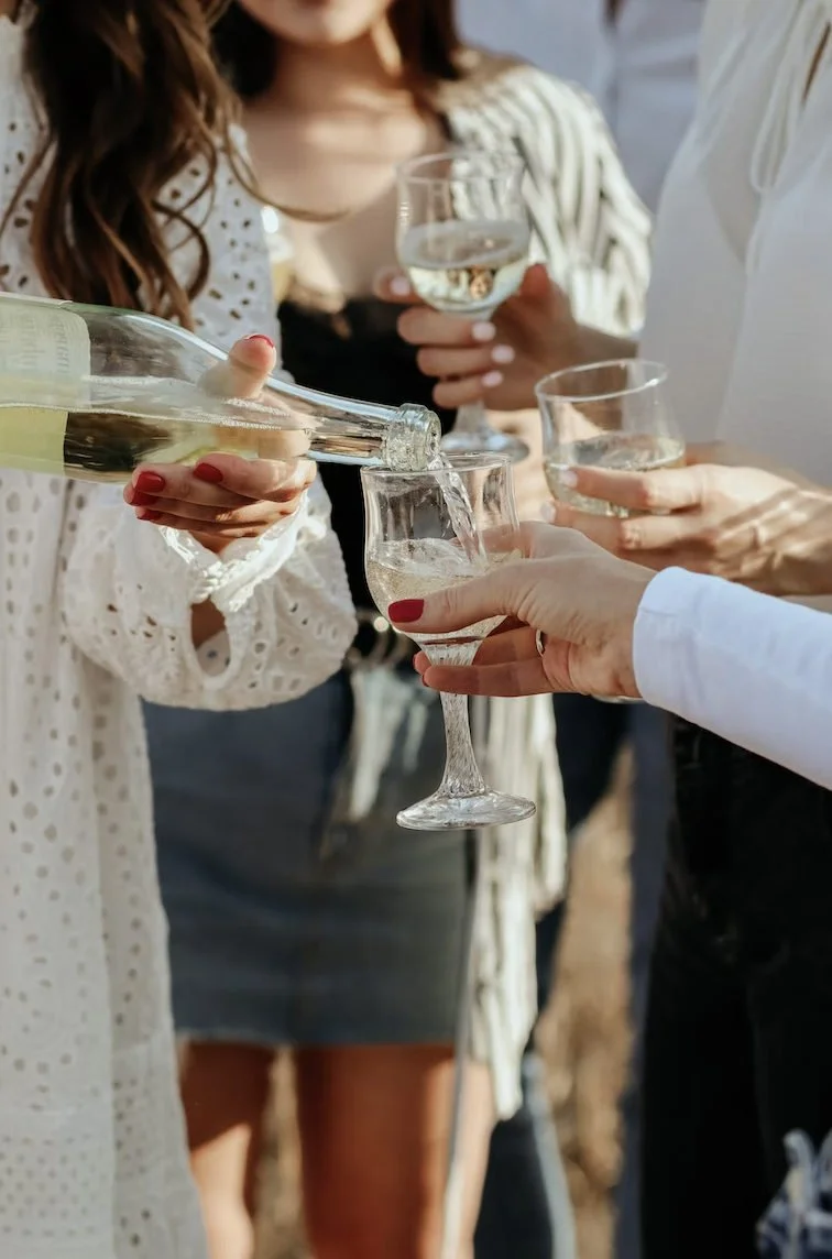 Friends pour white wine and gather their glasses for a toast.