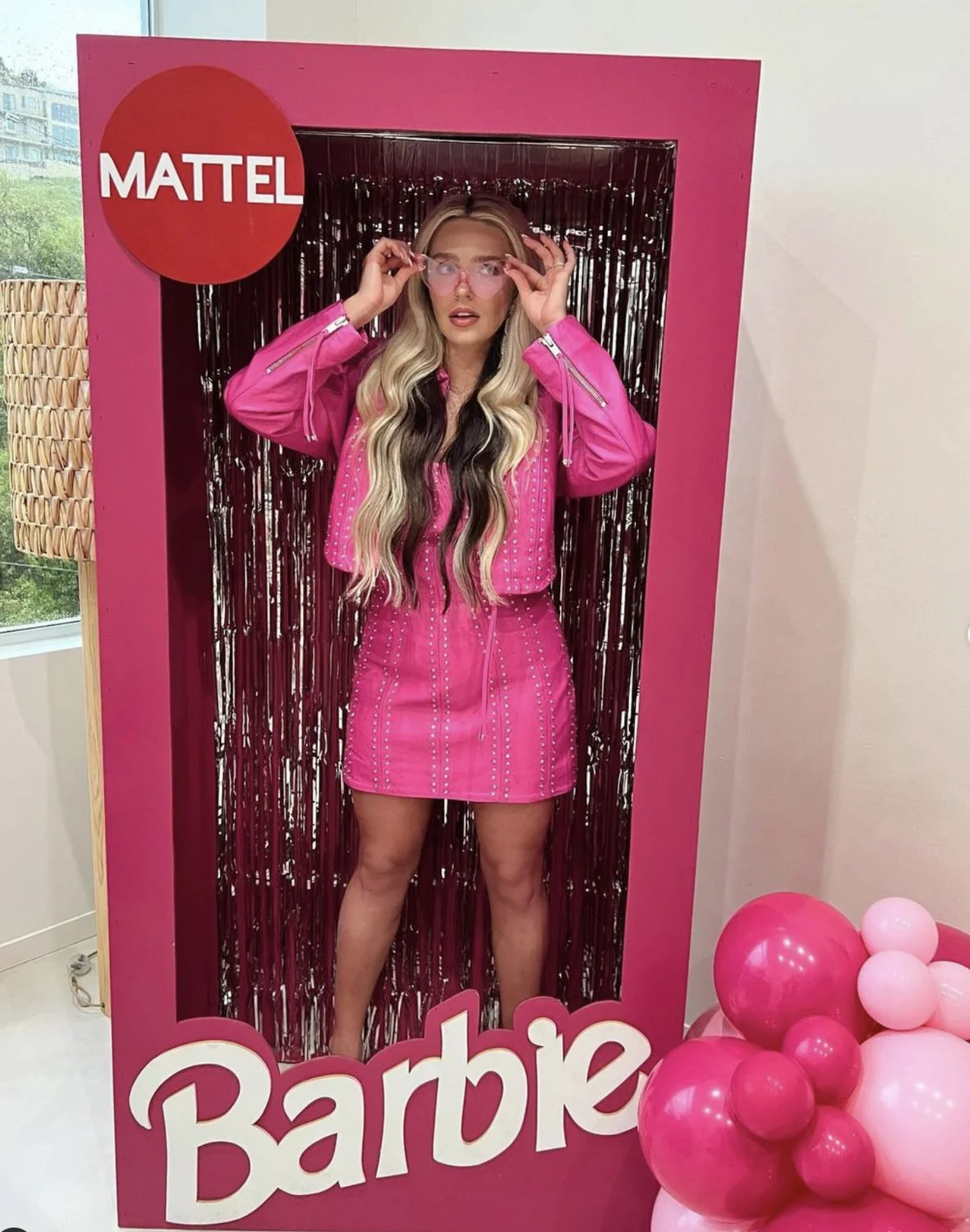 Woman in a pink dress and cowboy hat posing inside a life-size Barbie photo booth.