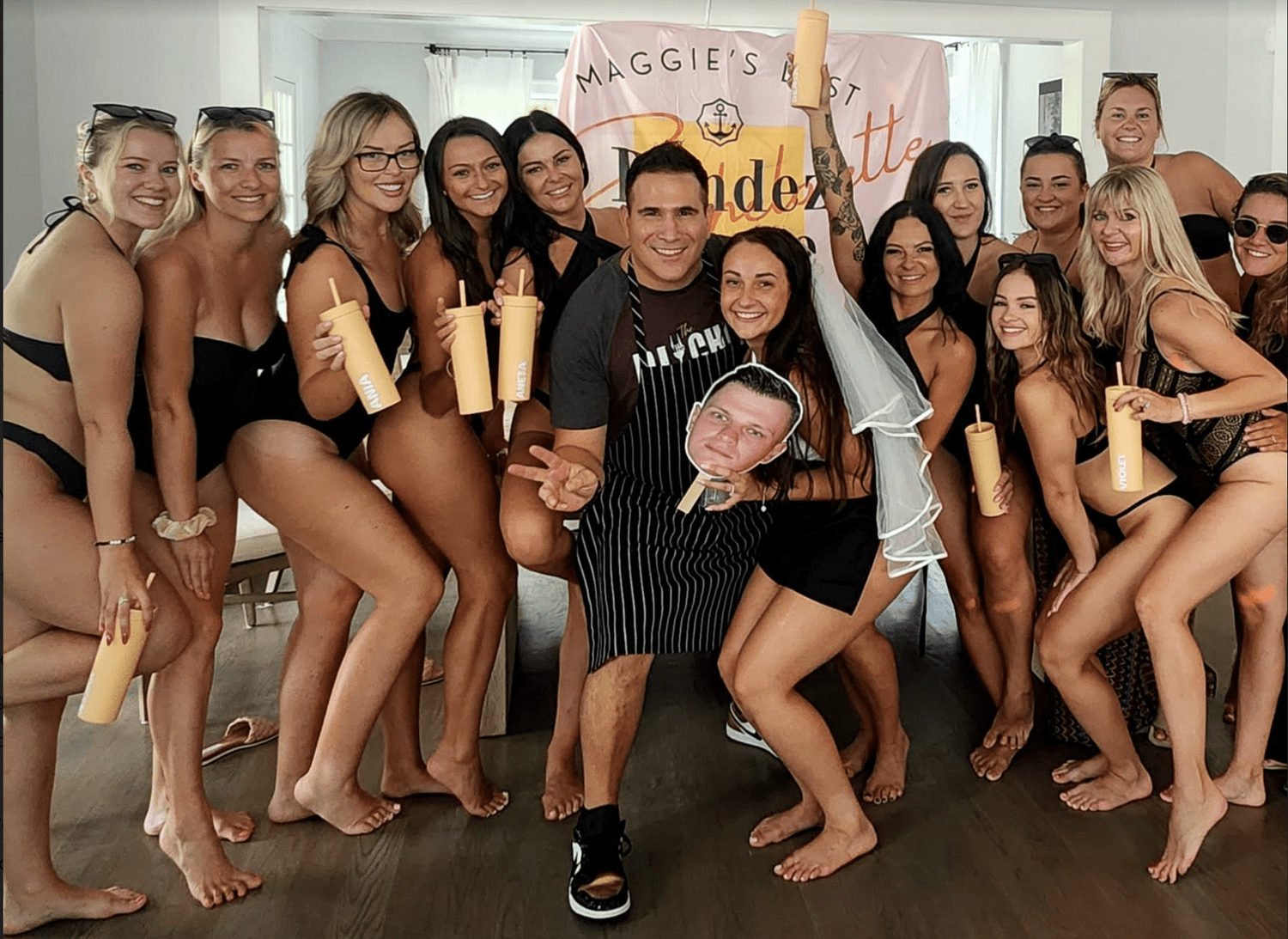 Bachelorette group posing with a private chef in a kitchen decorated with pink bride balloons.
