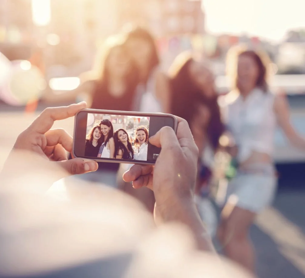 Friends posing together as someone takes their photo with a smartphone.