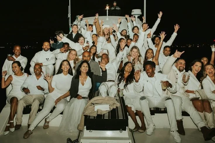 Friends in white outfits celebrating together on a boat at night.