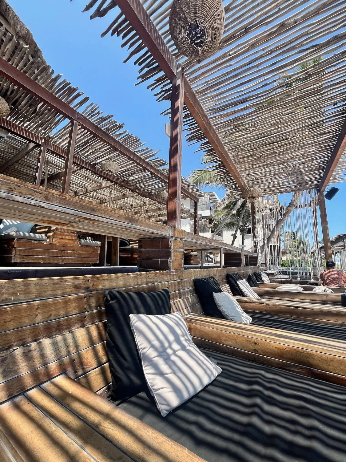 Cushioned wooden lounge seating beneath a slatted shade roof at Amansala in Tulum.
