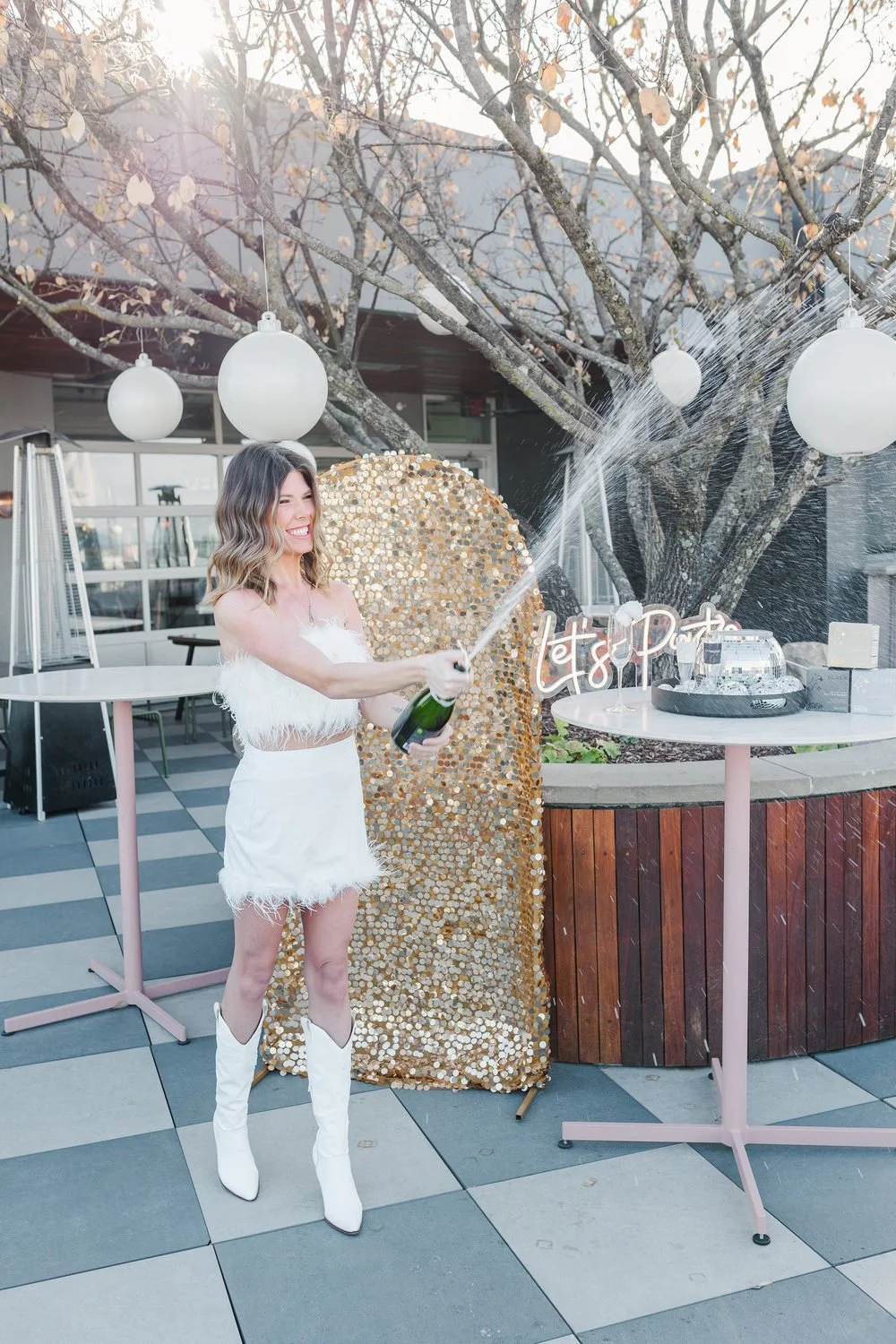 Woman in a white dress and boots posing beside a gold backdrop on the L.A. Jackson rooftop terrace.
