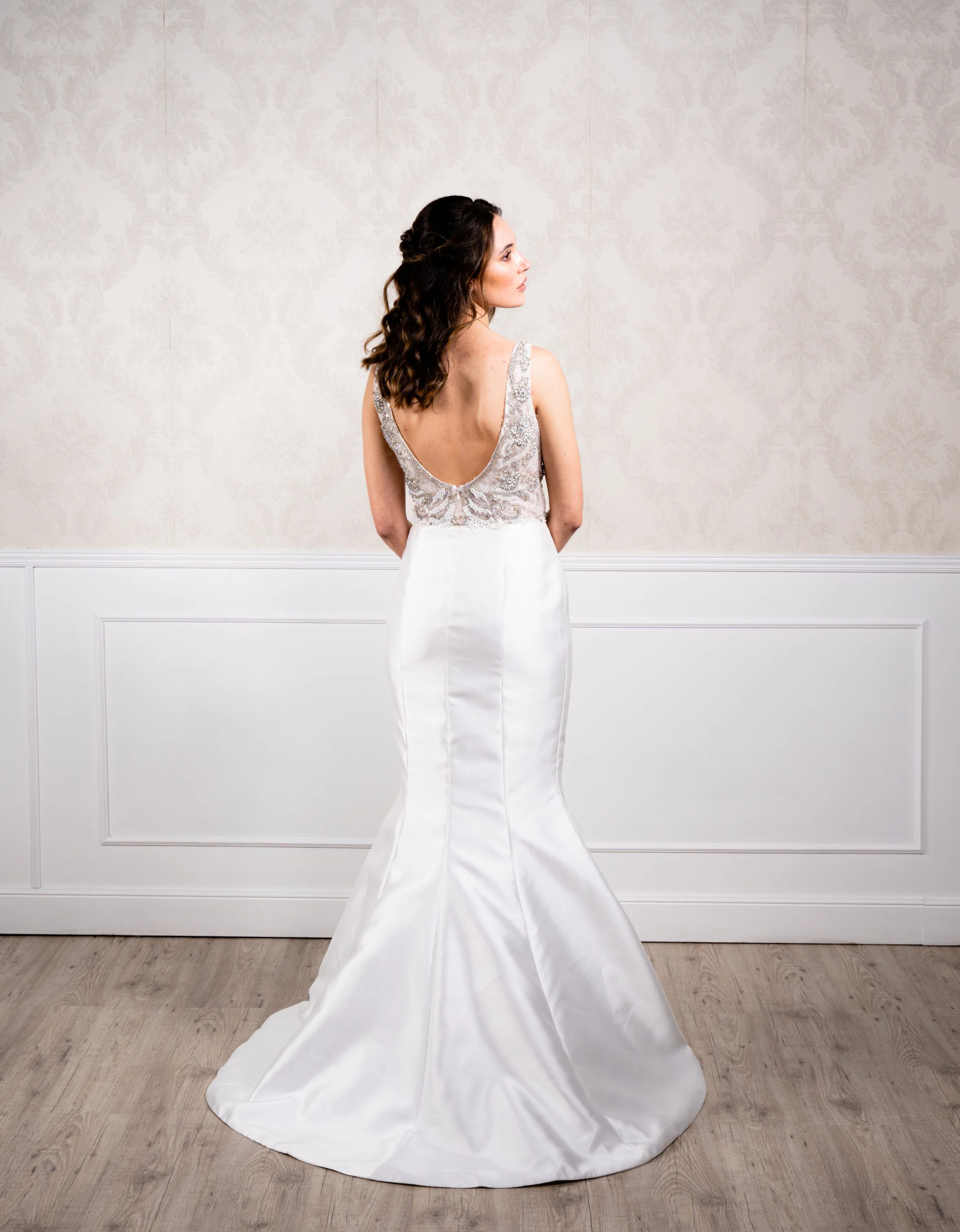 Vestido de silueta sirena elaborado con tafetán en la falda, tul bordado en pedrería plateada envejecida y pedrería blanca en el cuerpo, tirante ancho y espalda baja.