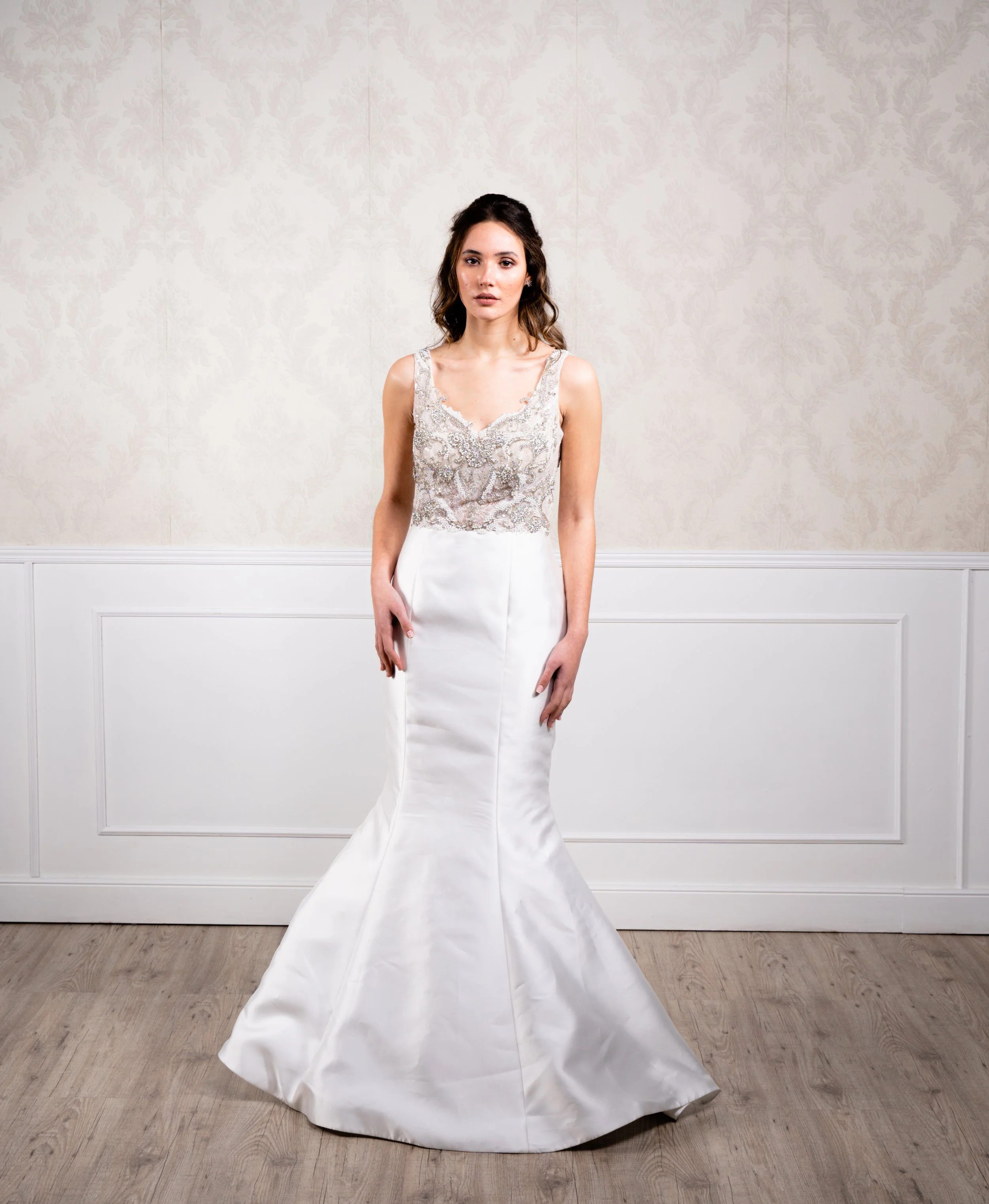 Vestido de silueta sirena elaborado con tafetán en la falda, tul bordado en pedrería plateada envejecida y pedrería blanca en el cuerpo, tirante ancho y espalda baja.