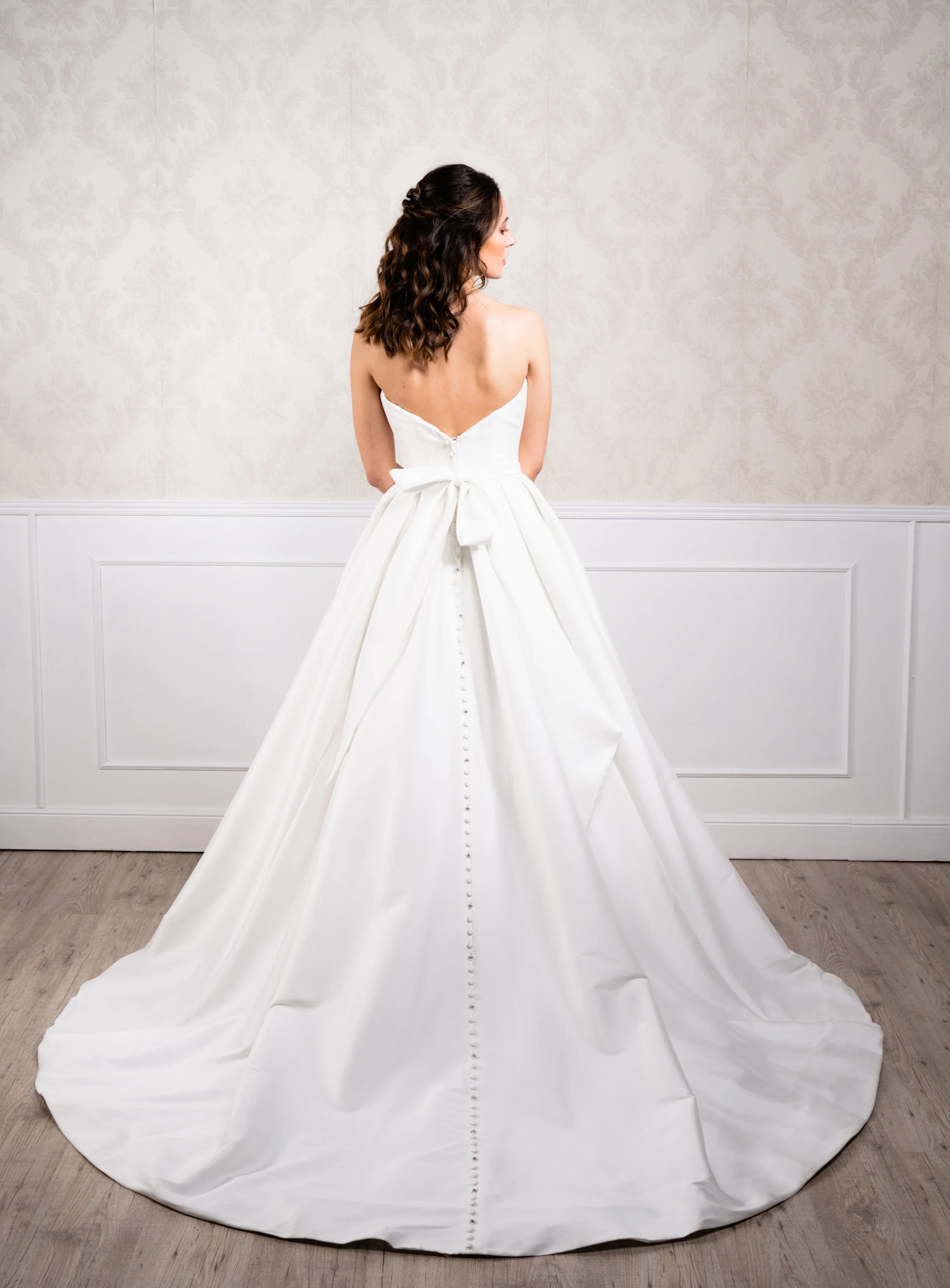 Vestido en forma de princesa elaborado en punto elástico suave, con escote de palabra de honor reforzado con corsé interior y botonadura decorativa hasta la cola.
