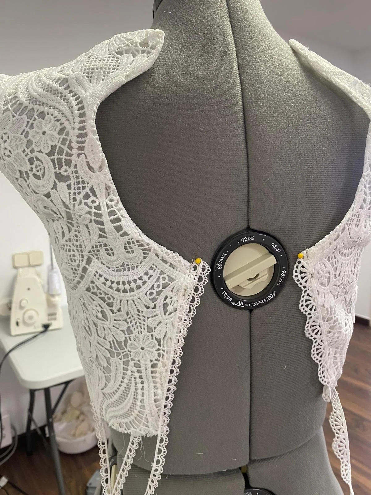 Maniquí sin cabeza con vestido de encaje blanco y una máquina para medir la altura en la espalda.