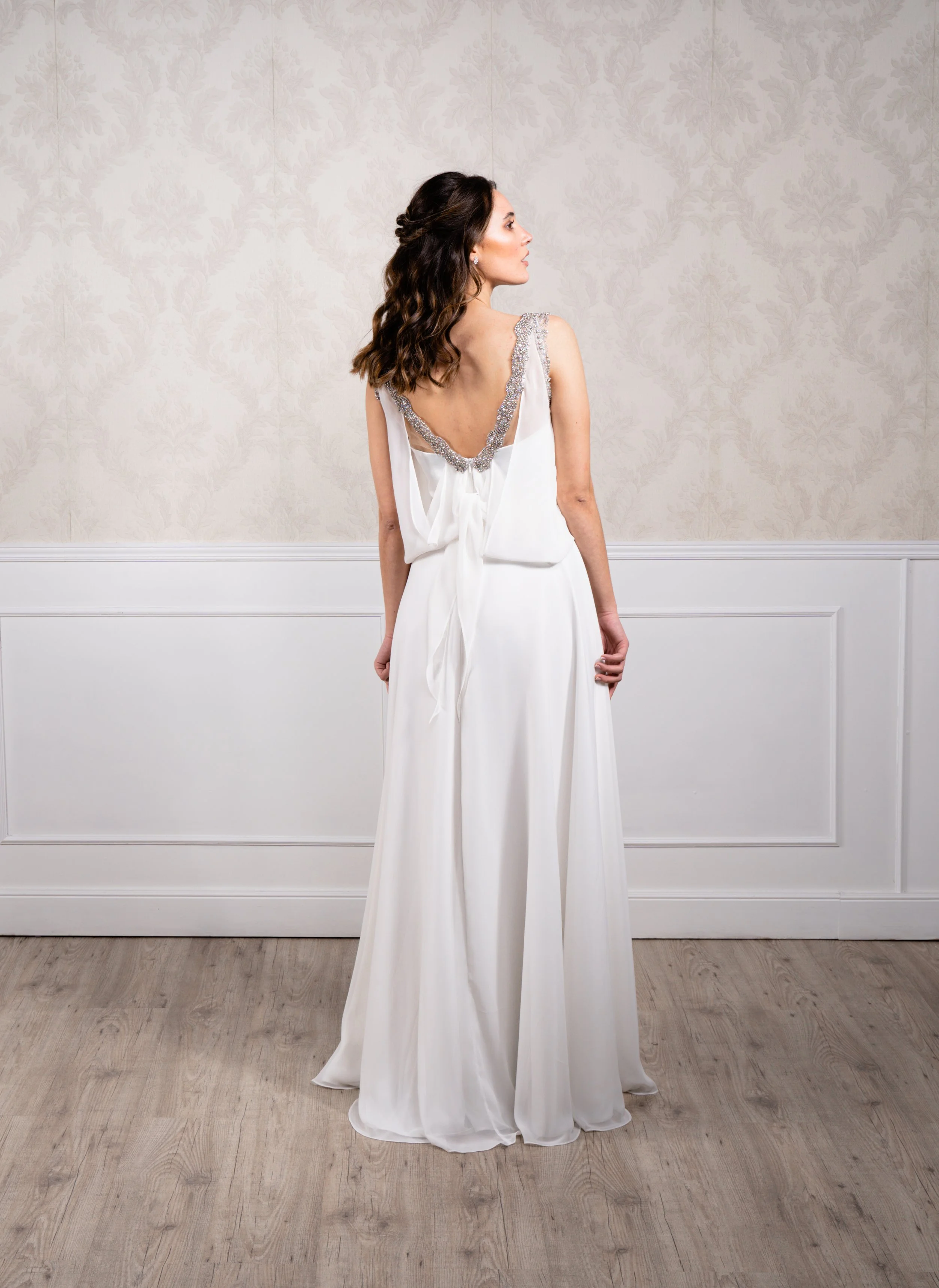 Vestido en silueta A elaborado en chiflón y gasa con corte inspiración griego, detalles de cristal envejecido en escote y espalda.