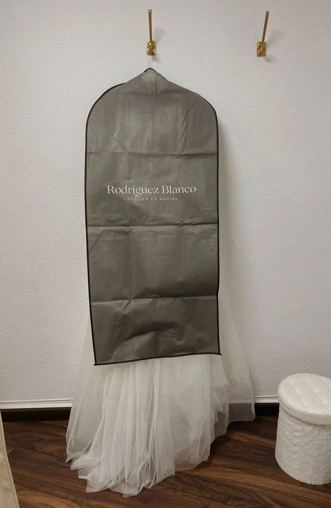 Bolsón de polvo para vestidos de novia en una habitación, con el logo 'Rodríguez Blanco Atelier de Novias' impreso en él, colgado en la pared