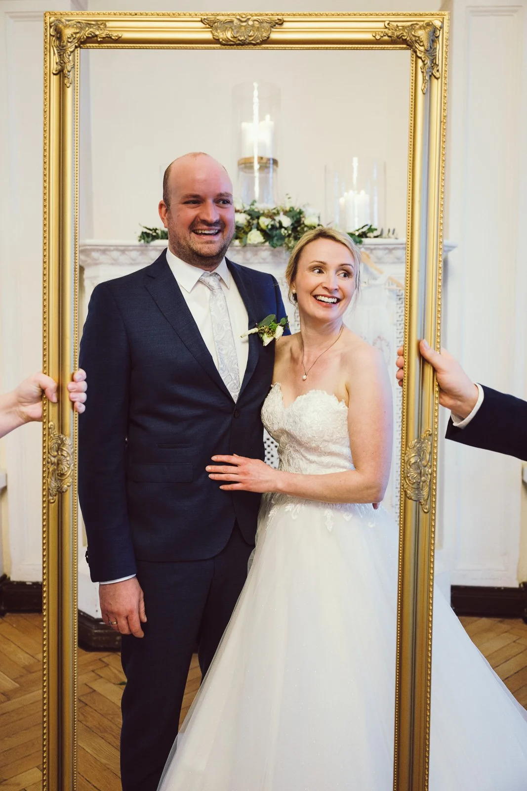 Ein glückliches Brautpaar in Hochzeitskleidung, sichtbar innerhalb eines großen, goldenen Rahmen gehalten, bei einer Hochzeitsfeier.