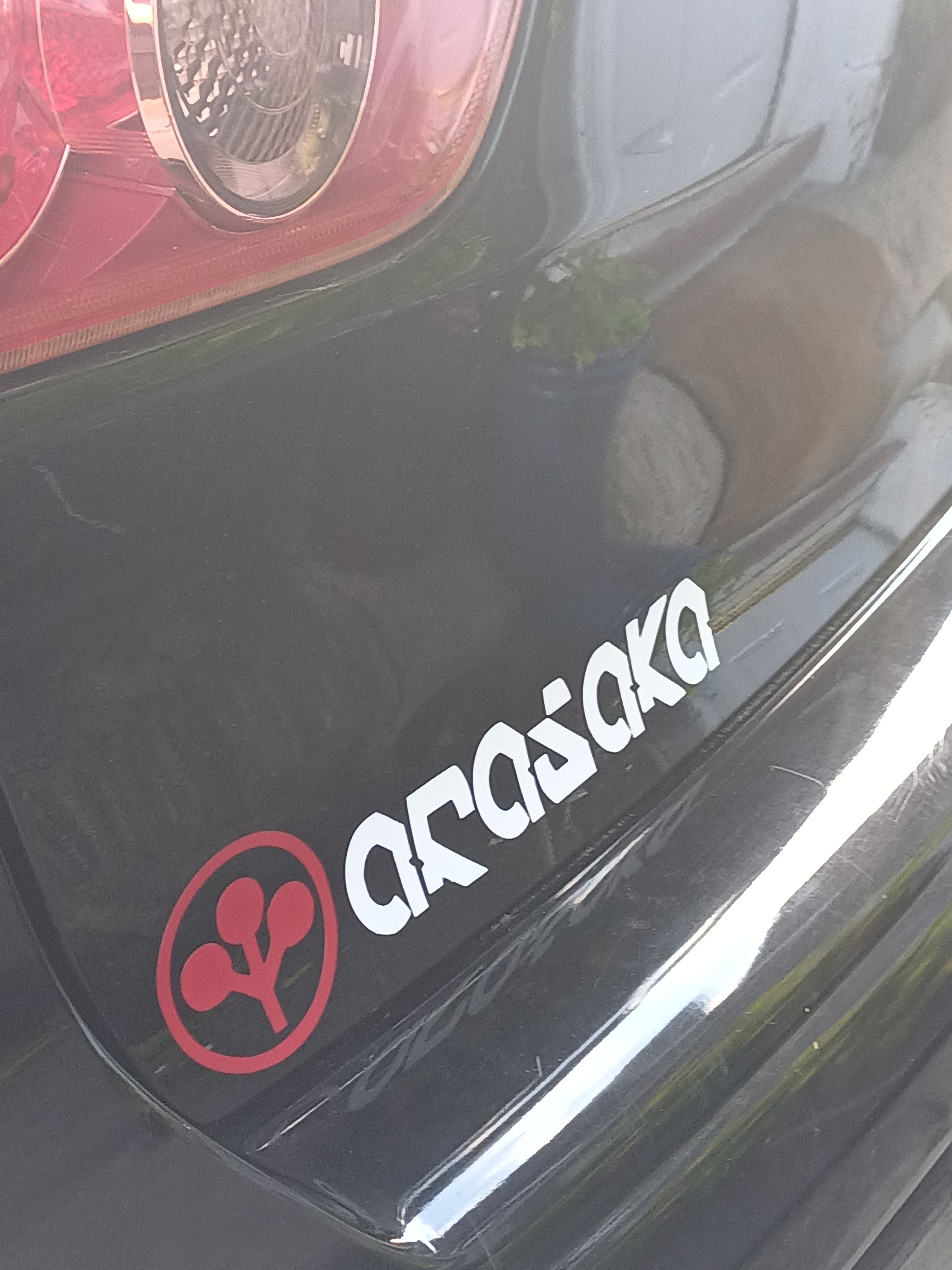 Close-up of the rear part of a black Mitsubishi JDM  vehicle with a red sticker on the back. The Arasaka  logo is visible