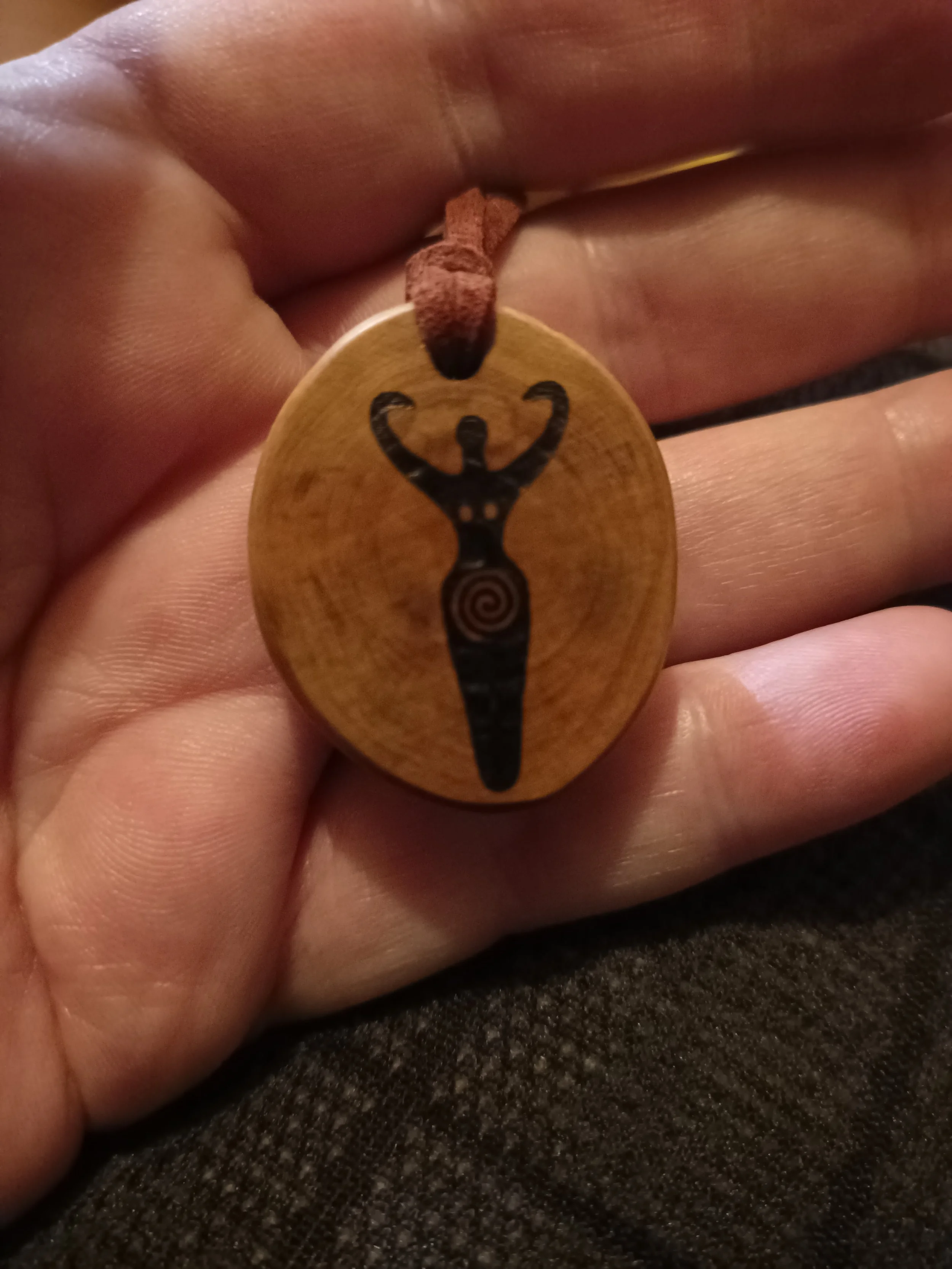 A wooden pendant with a Fertillity Symbol design  