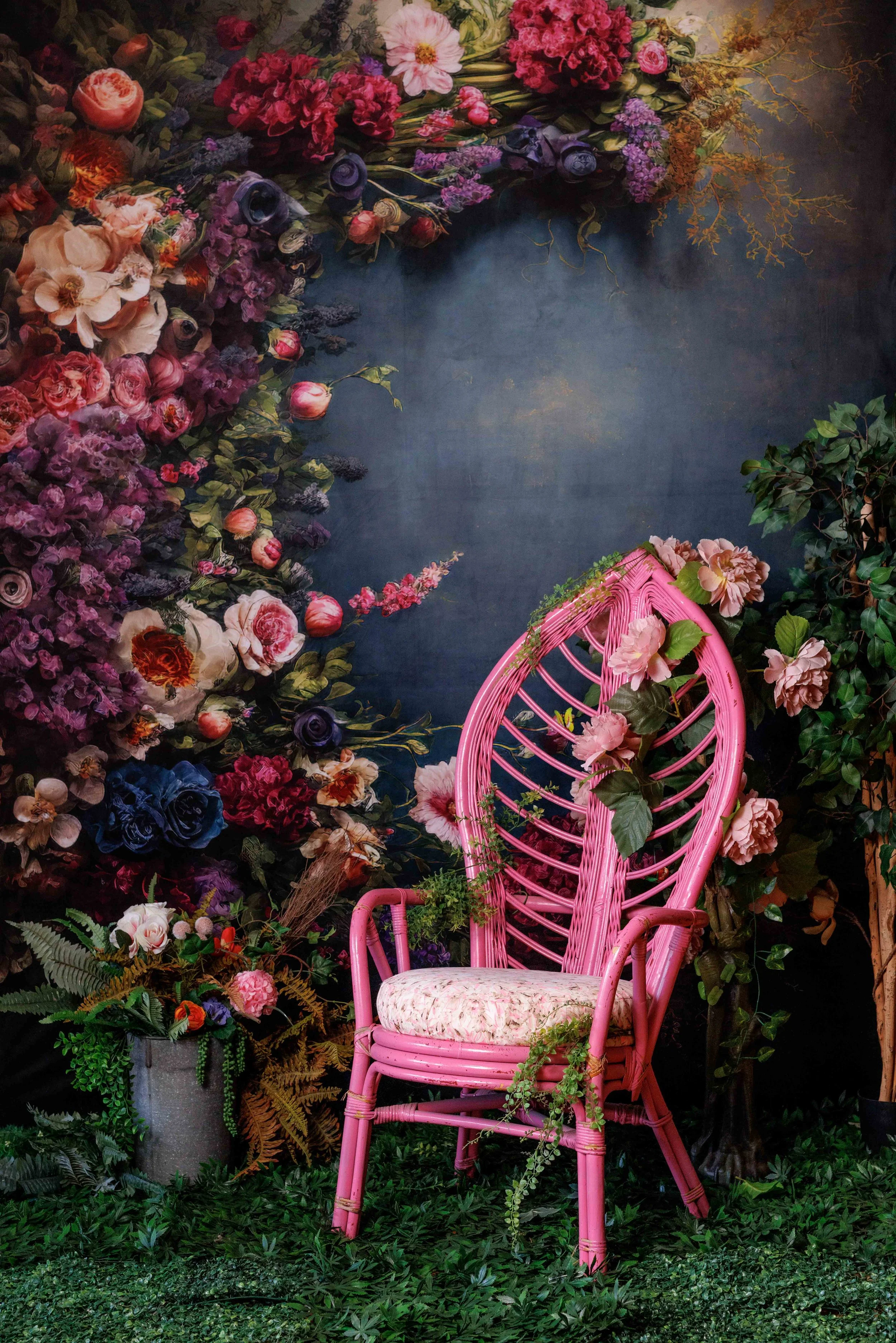 Floral photography set with pink wicker chair, lush flowers, greenery, and dark textured backdrop, ideal for editorial and portrait photography